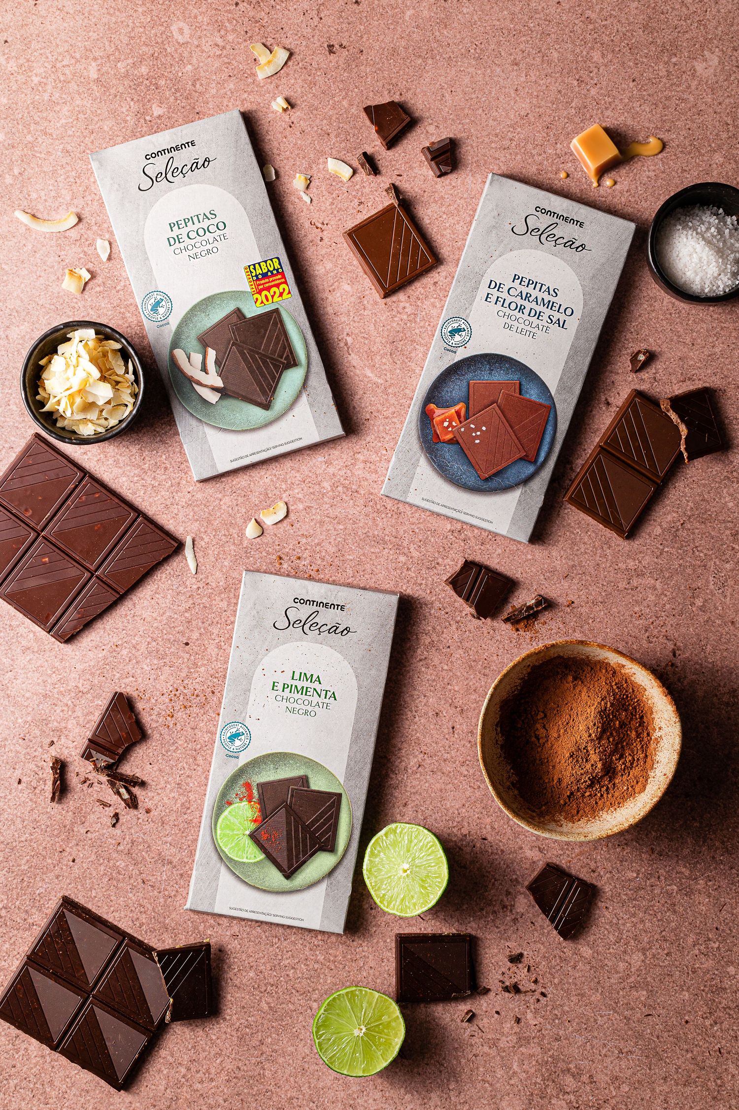 Artisanal chocolate bars with lime slices and cocoa powder on a pink surface.