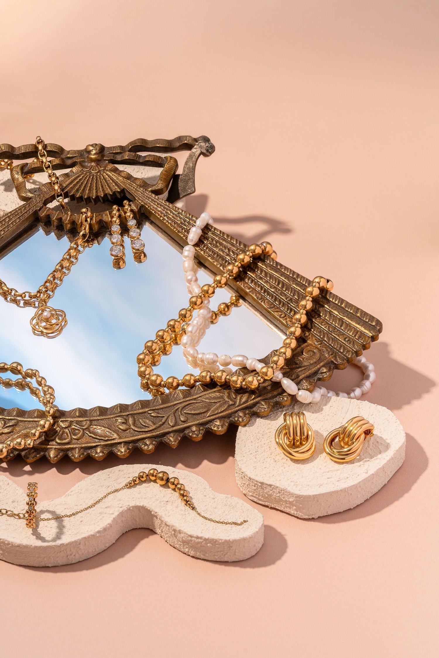 Ornate golden jewelry with fan-shaped pendants displayed on a peach background.