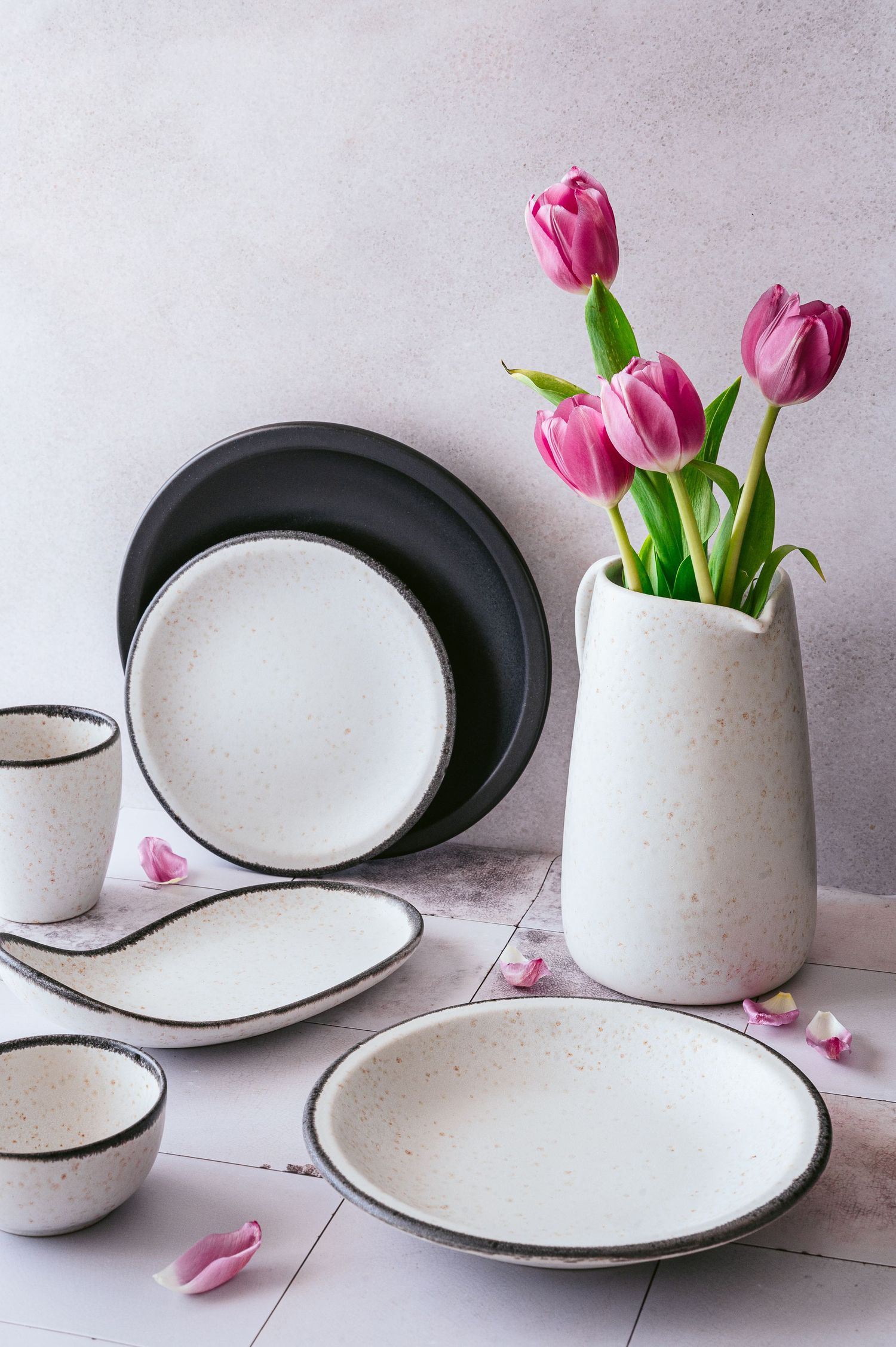 Modern white ceramic dinnerware set with pink tulips in minimalist vase.