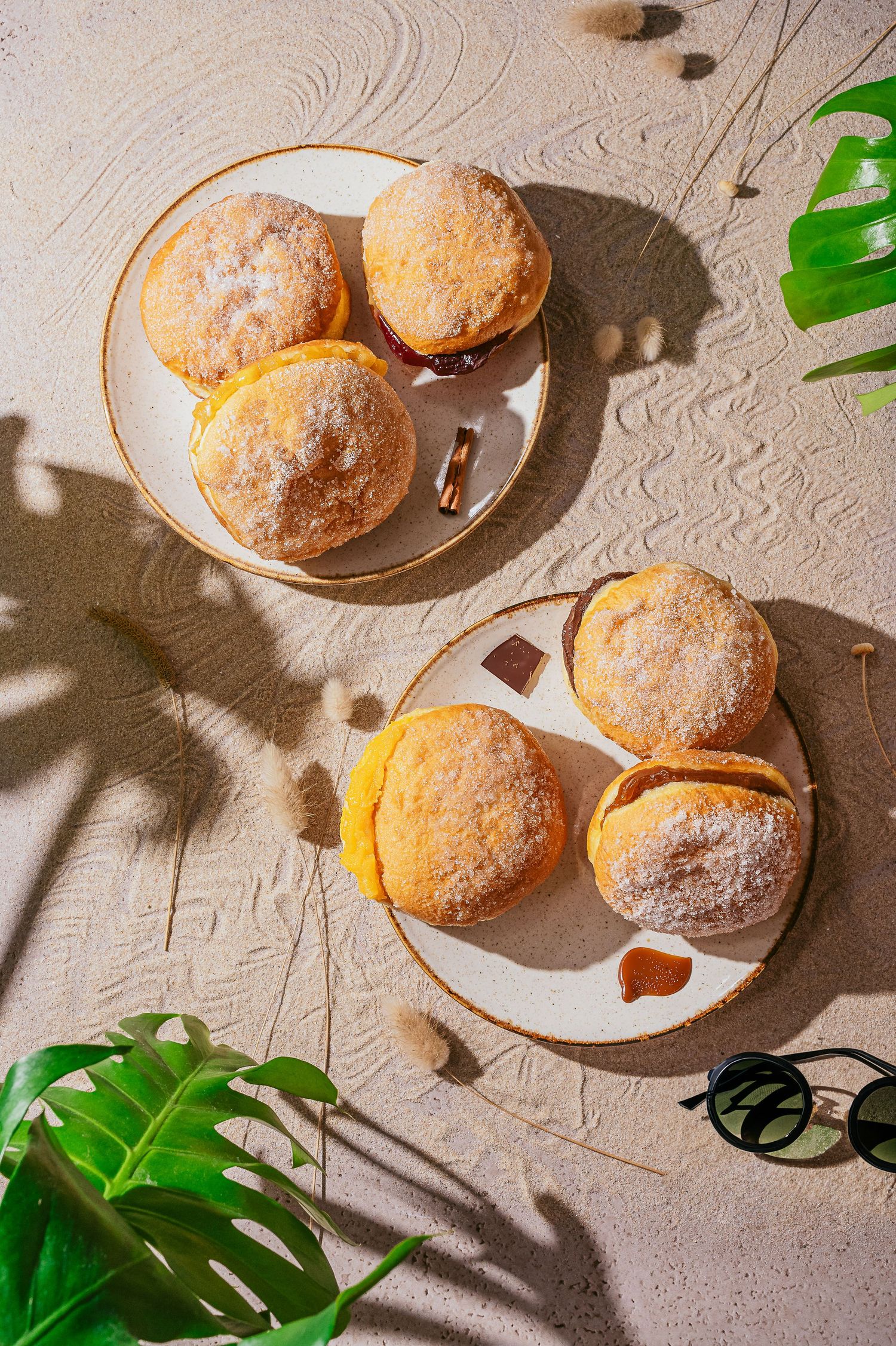 Sugar dusted donuts on white plates with tropical plant shadows.