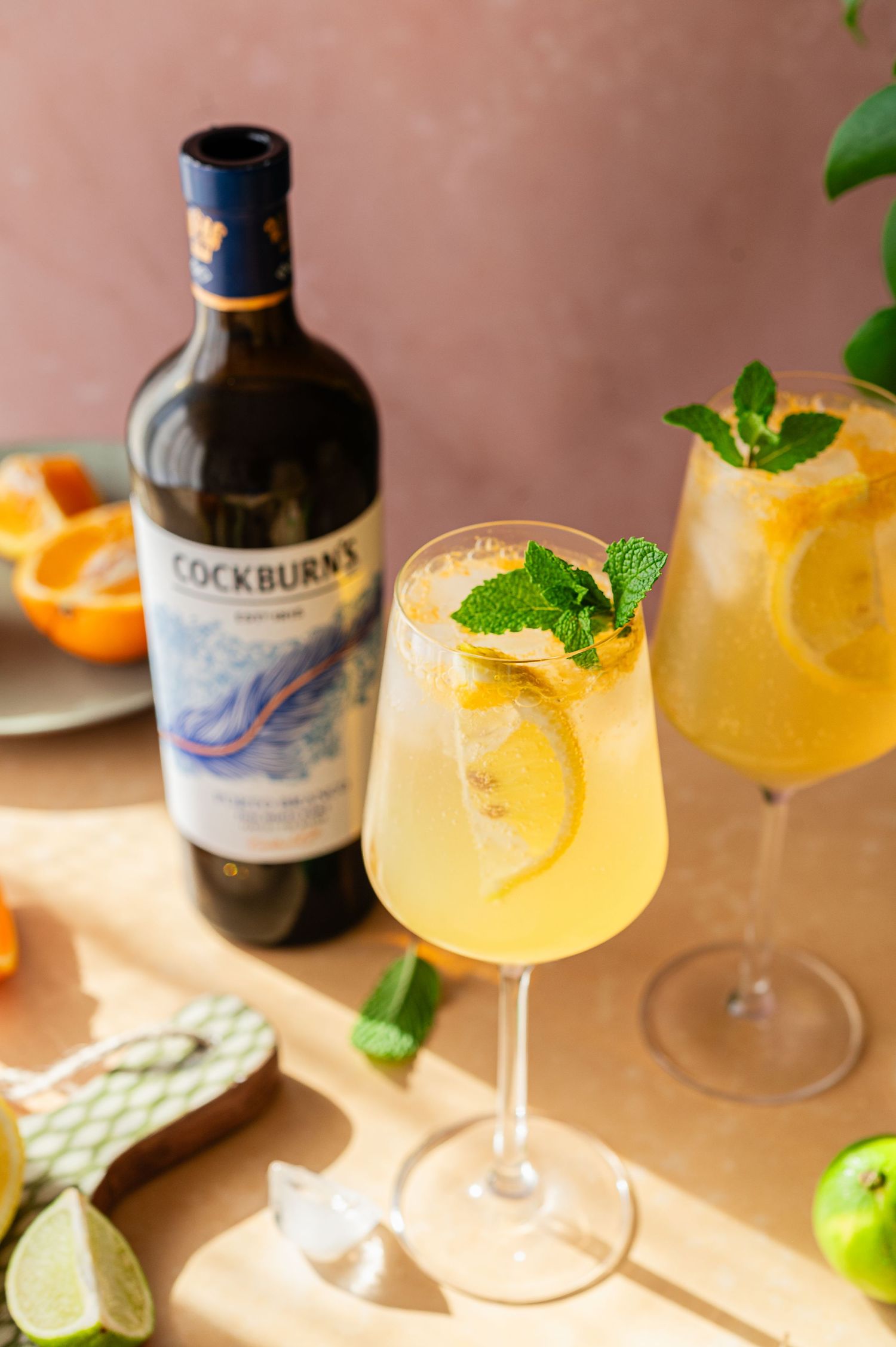 Refreshing citrus cocktails with mint garnish and Cockburn's bottle on a wooden surface.
