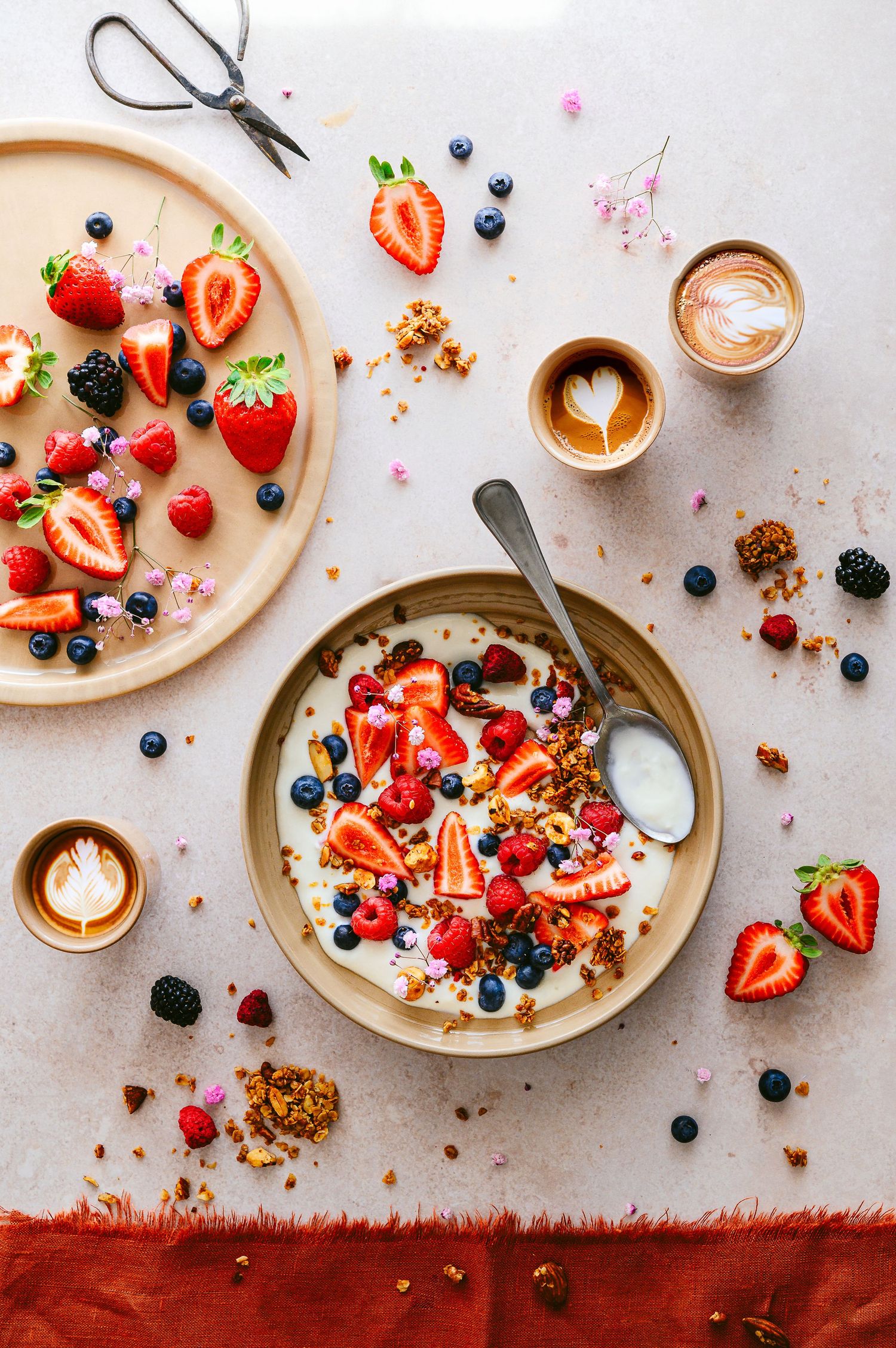 Colorful breakfast bowls with fresh berries, granola and yogurt styled on a light background.