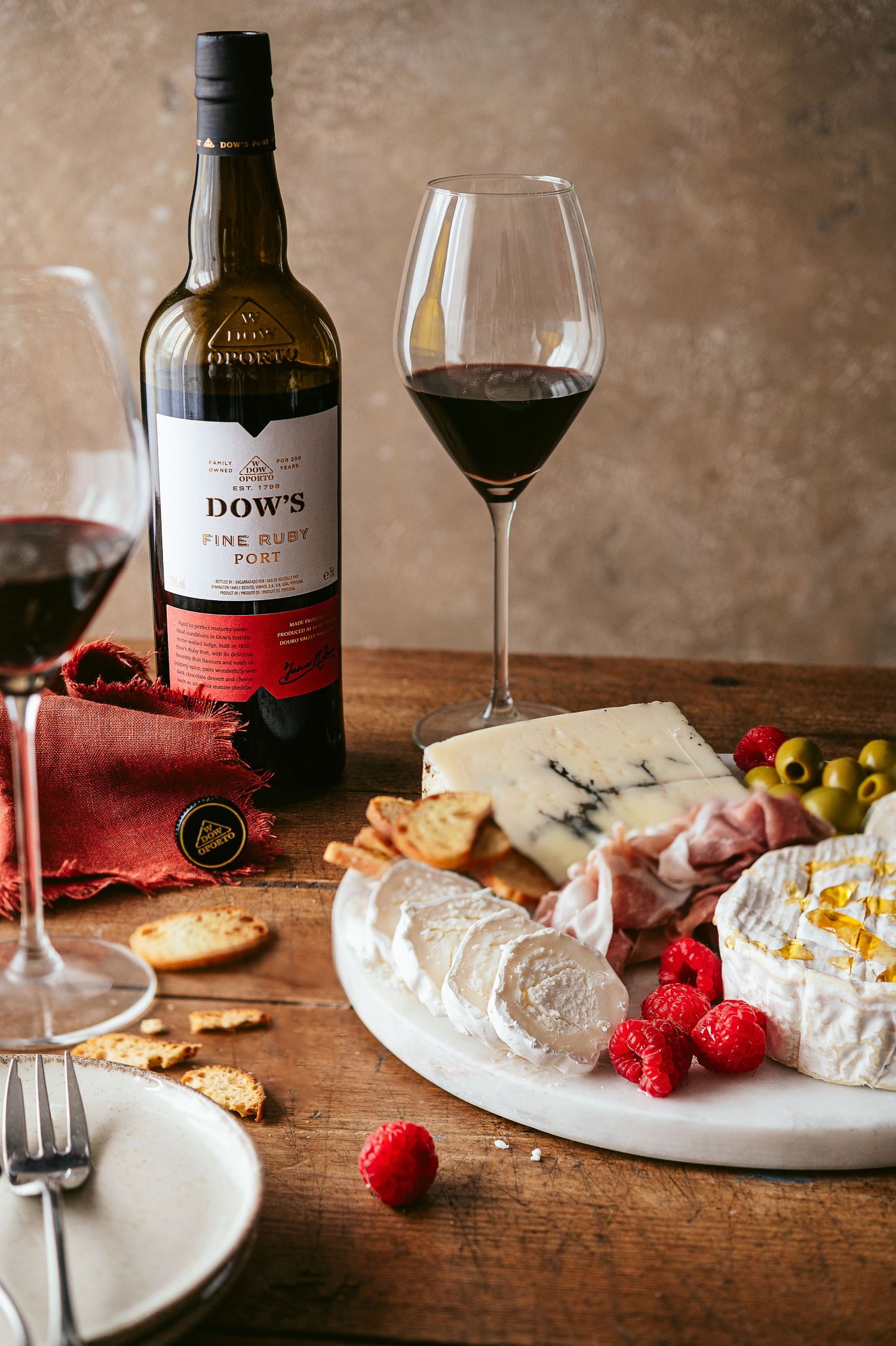 Charcuterie board with wine, cheese, raspberries and crackers on a rustic wooden table.