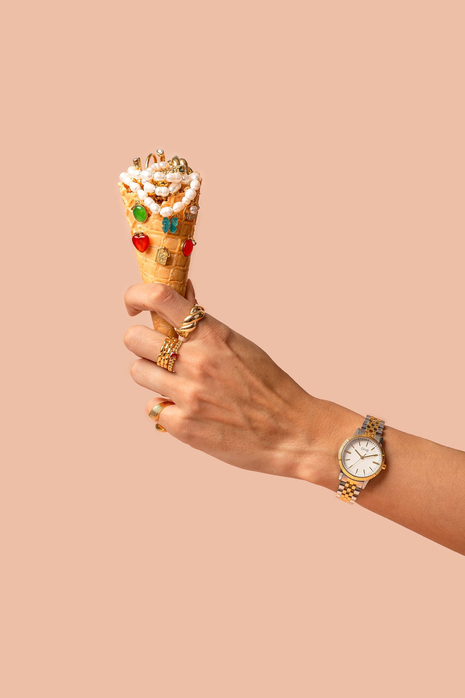 Hand holding decorated ice cream cone against peachy pink background.