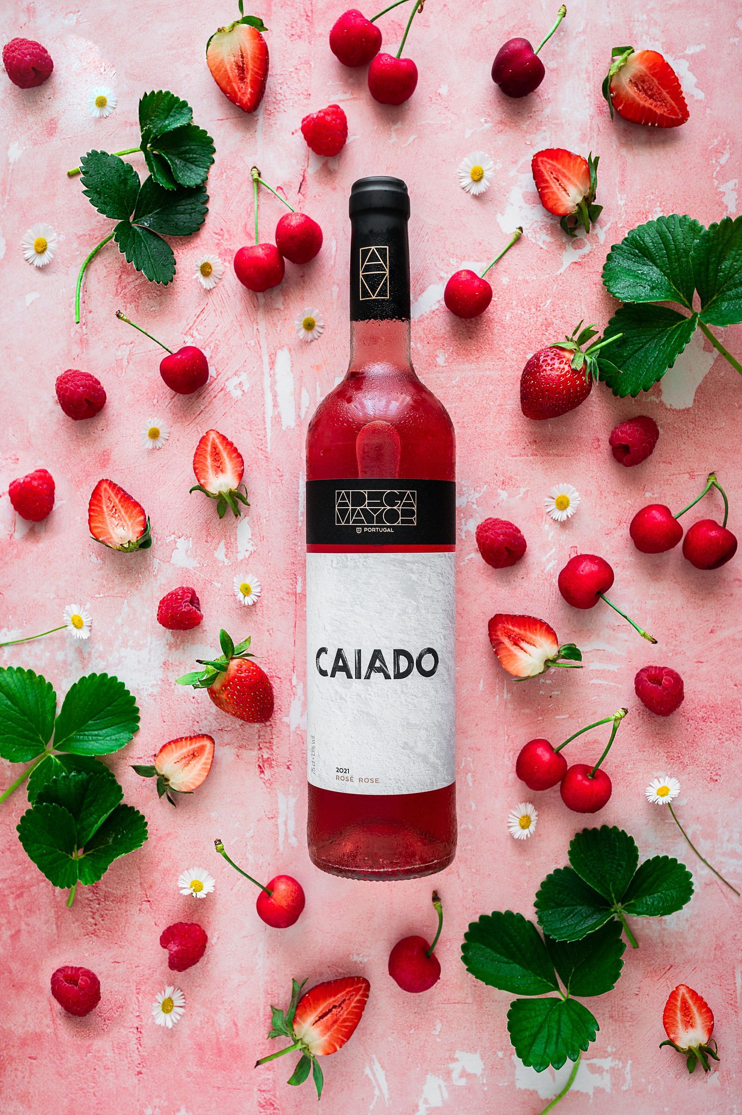 Pink flatlay with fresh cherries, strawberries, and a bottle of Caiado wine.