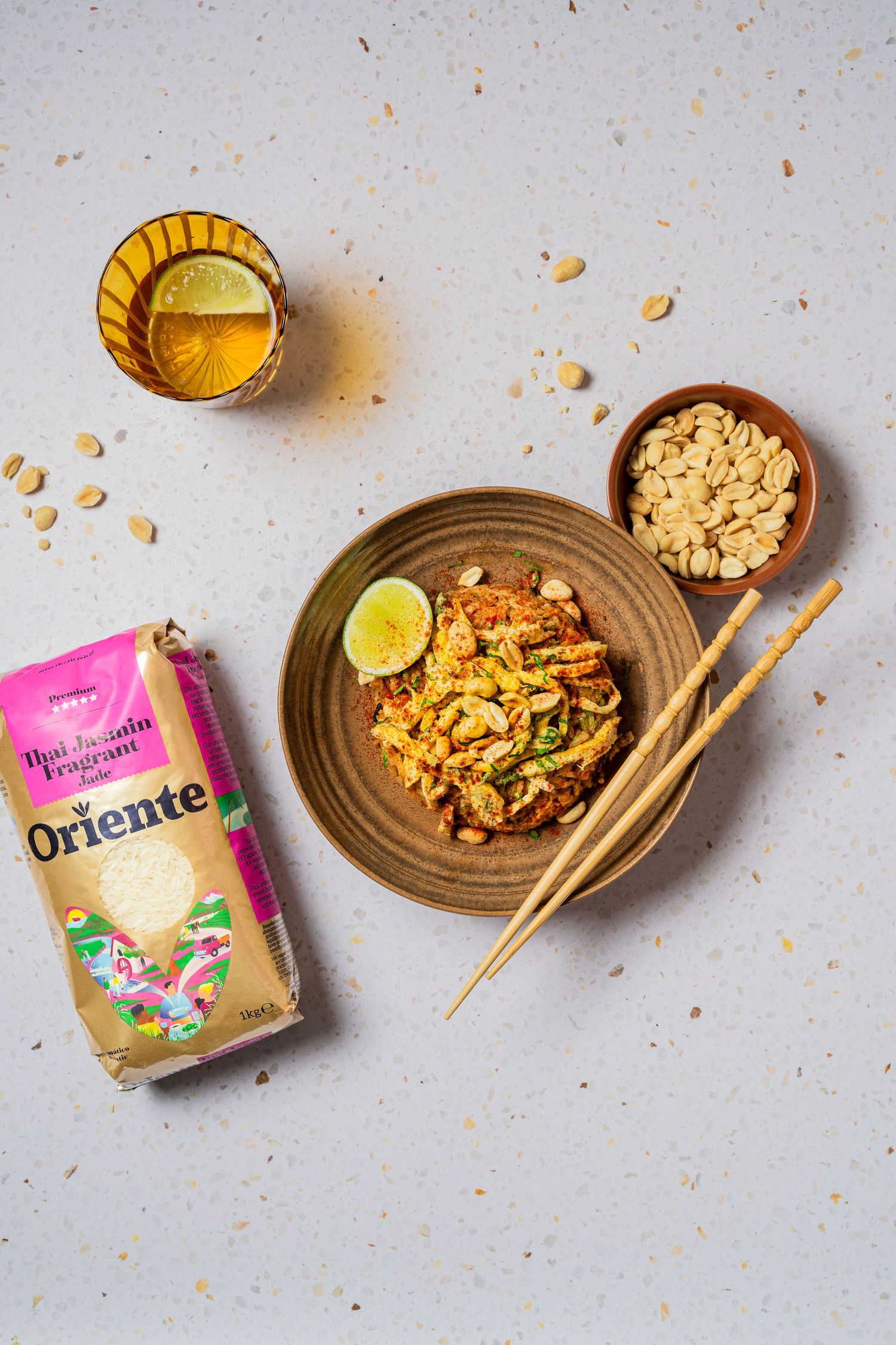 Asian noodle dish with chopsticks, nuts and beverage on light background.