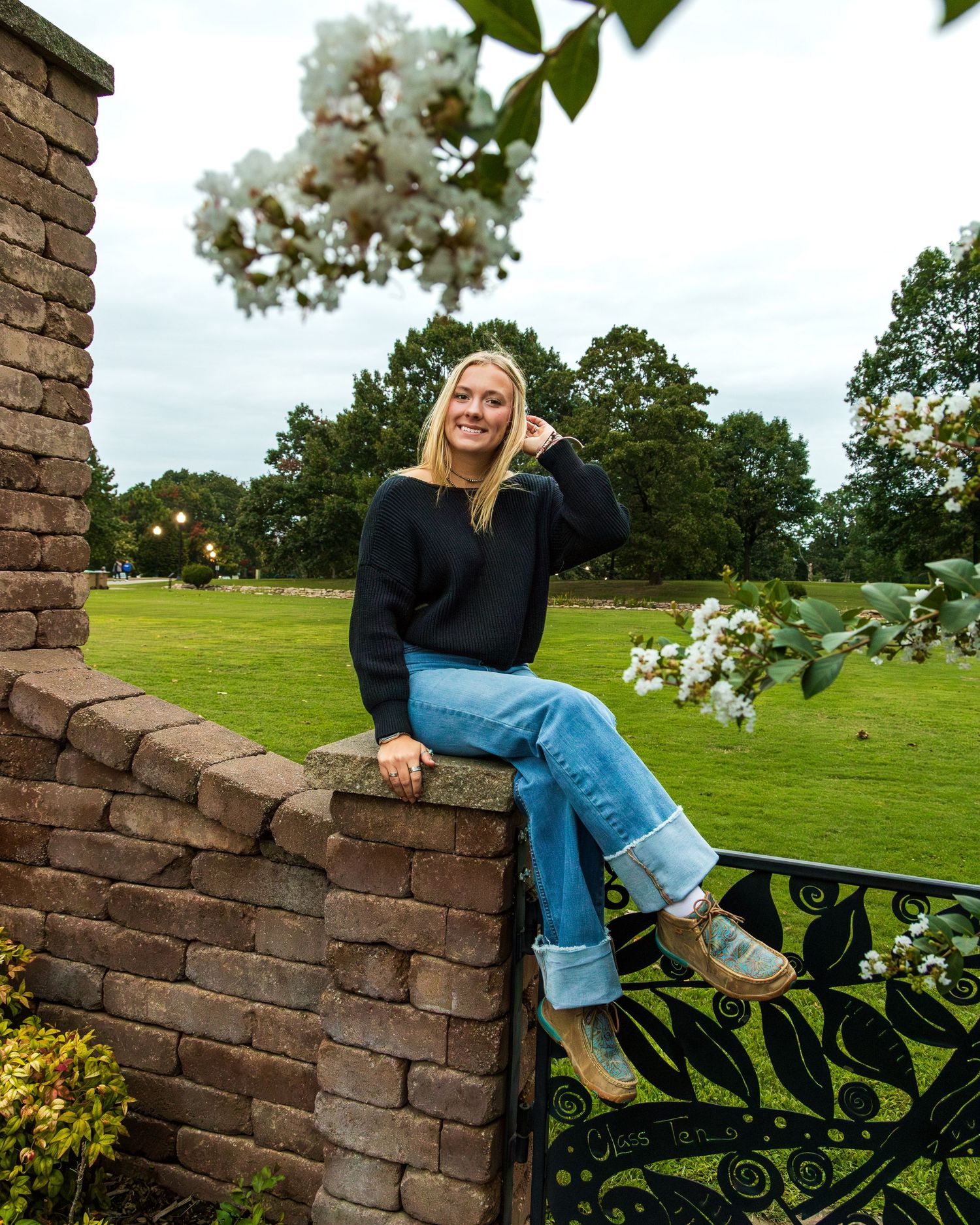 A girl sitting on a brick fence, playing with her hair.