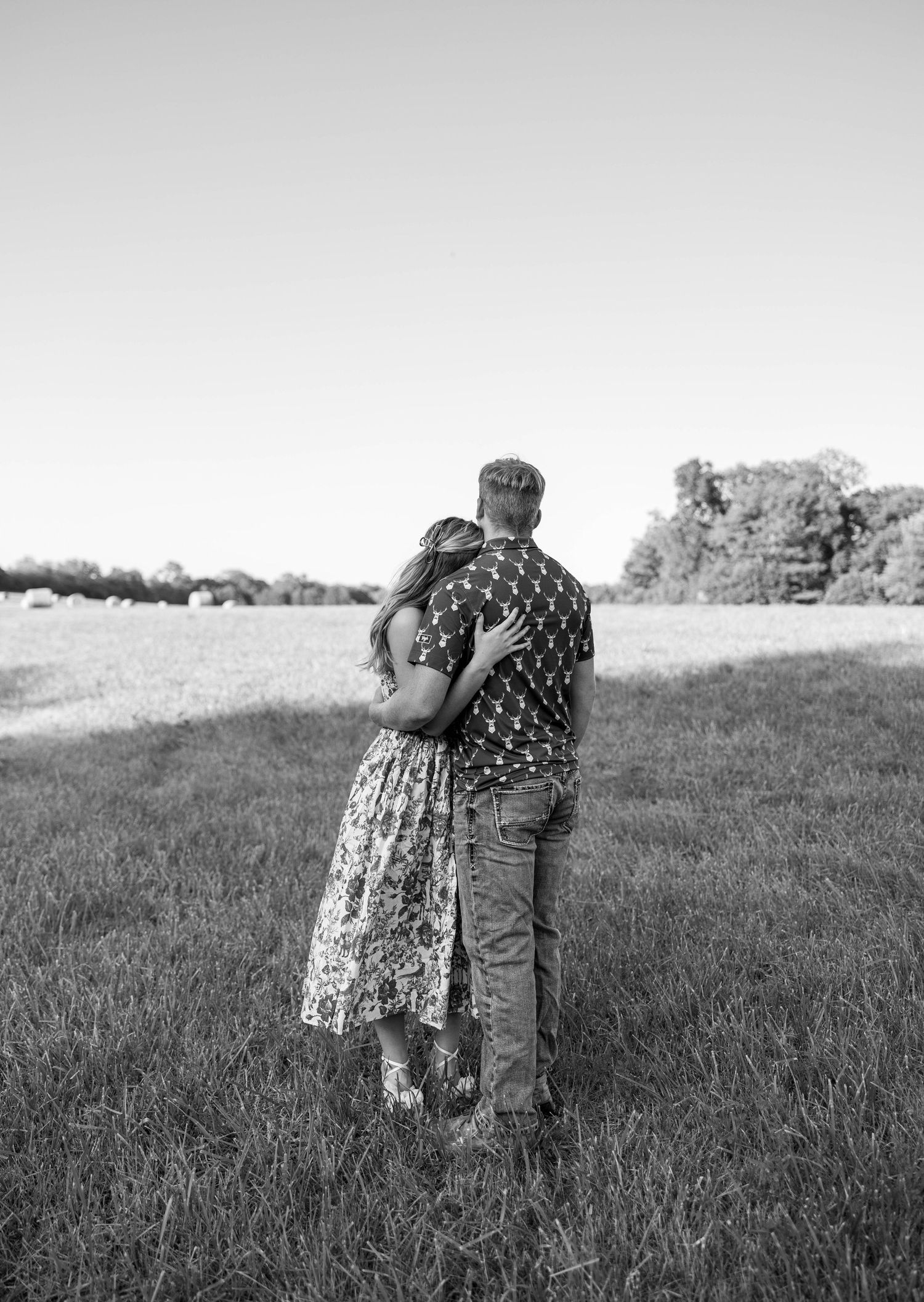 A couple hugging in a pasture.