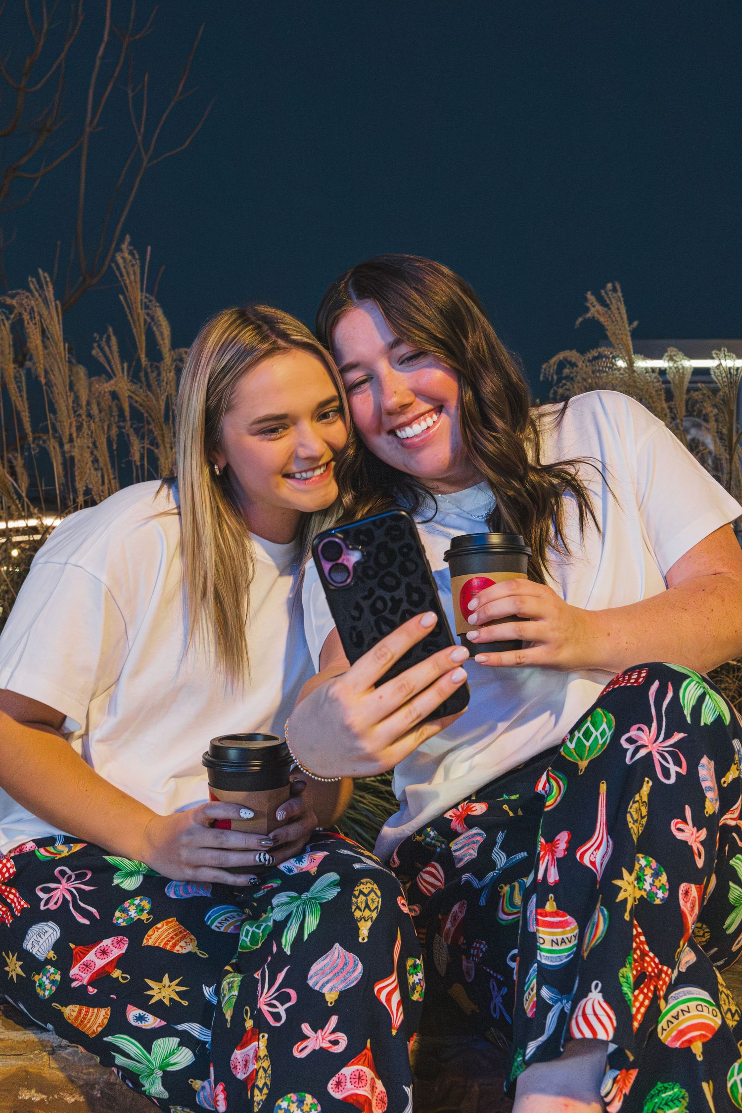 Two girls in Christmas PJs with coffees, taking a selfie.