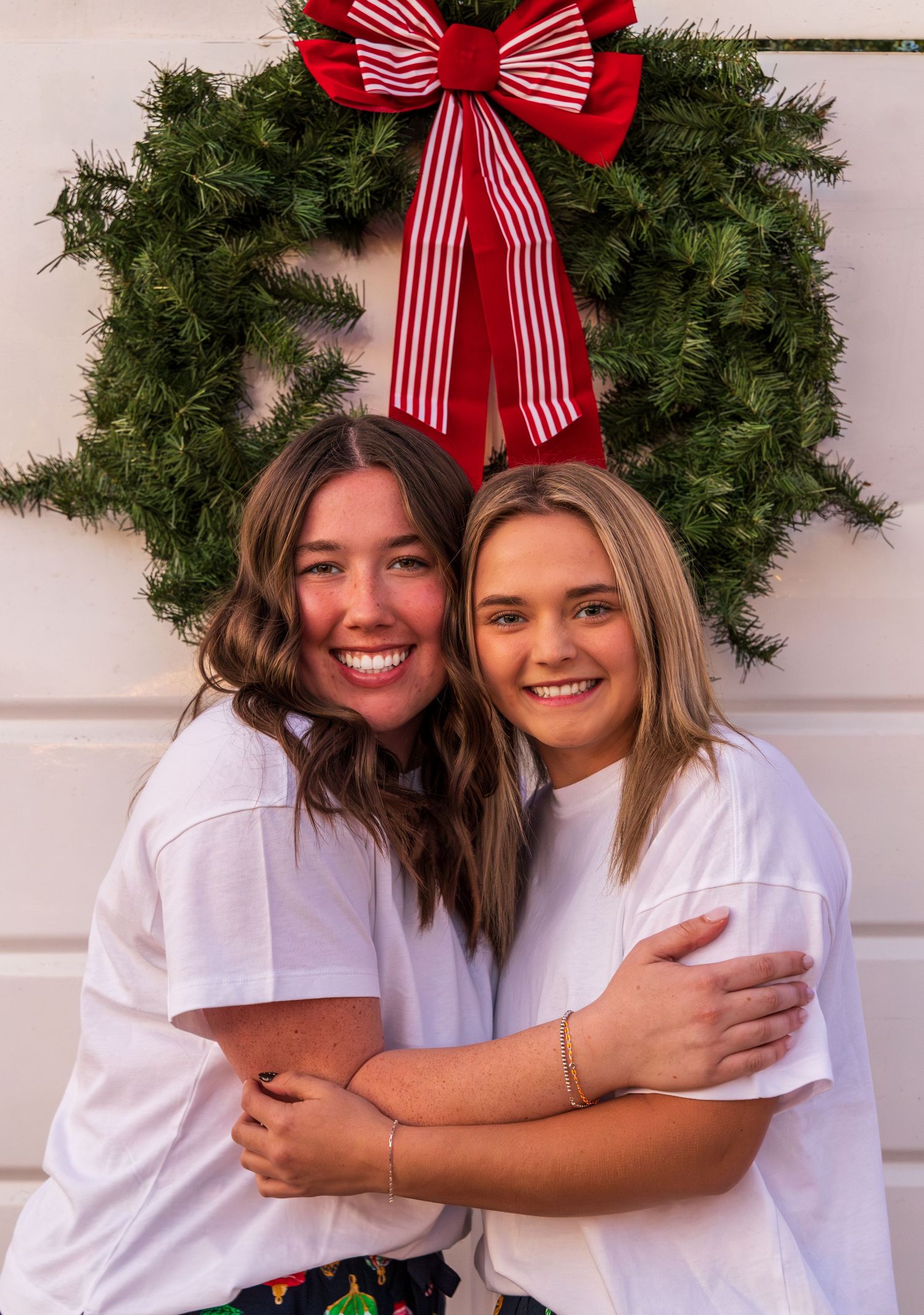 Two girls hugging and smiling in front of a trailer with a Christmas wreath on it.