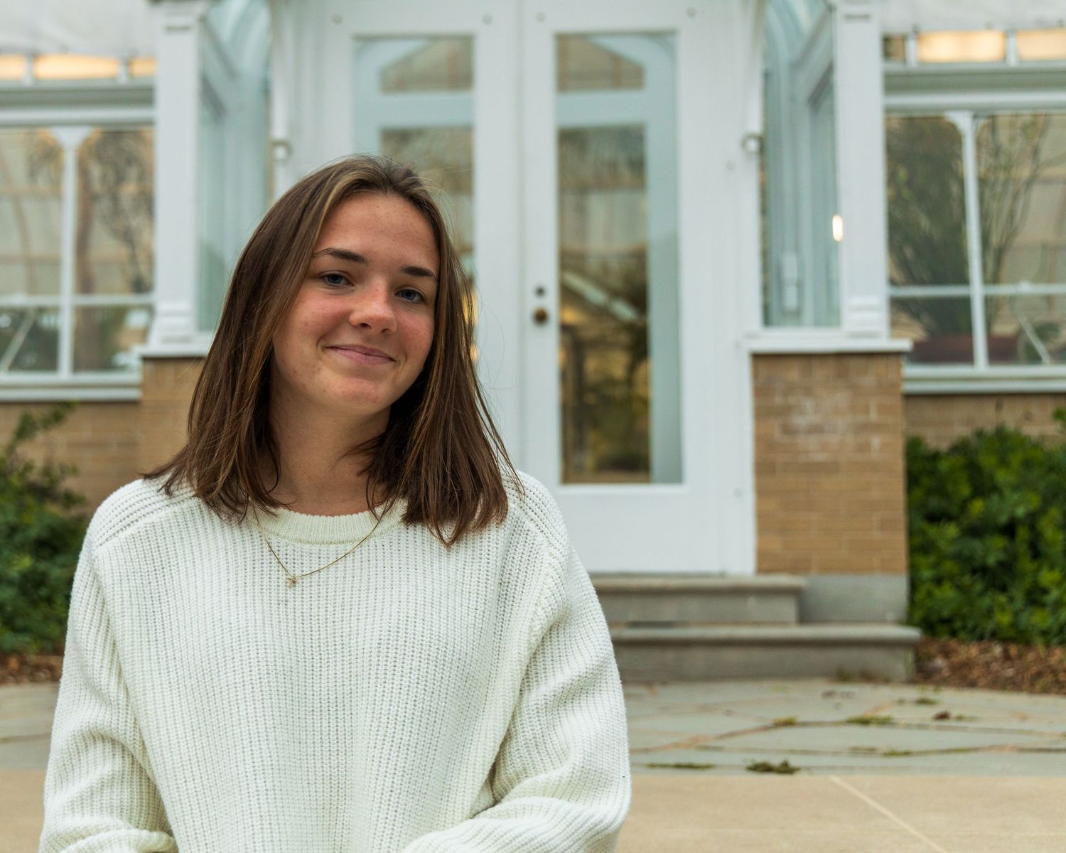 A girl sitting on stairs in front of a greenhouse.