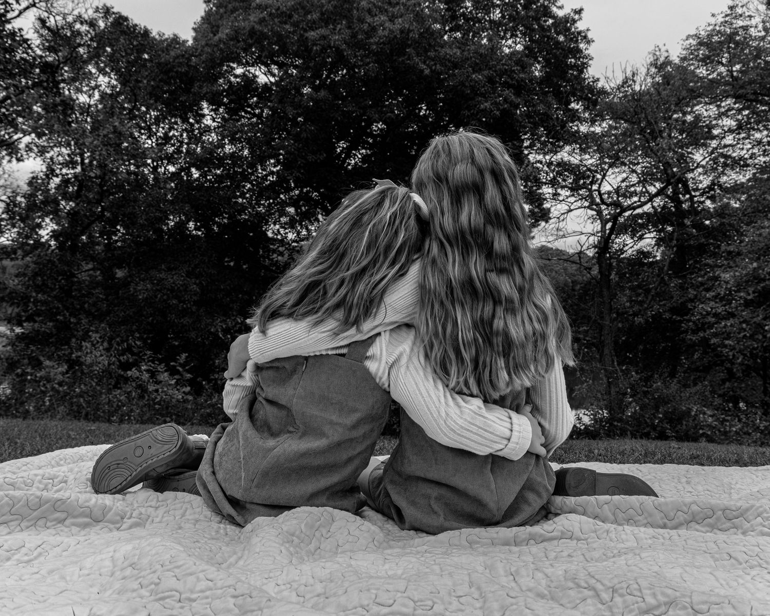 Two little girls with there arms around each other looking off into the distance.