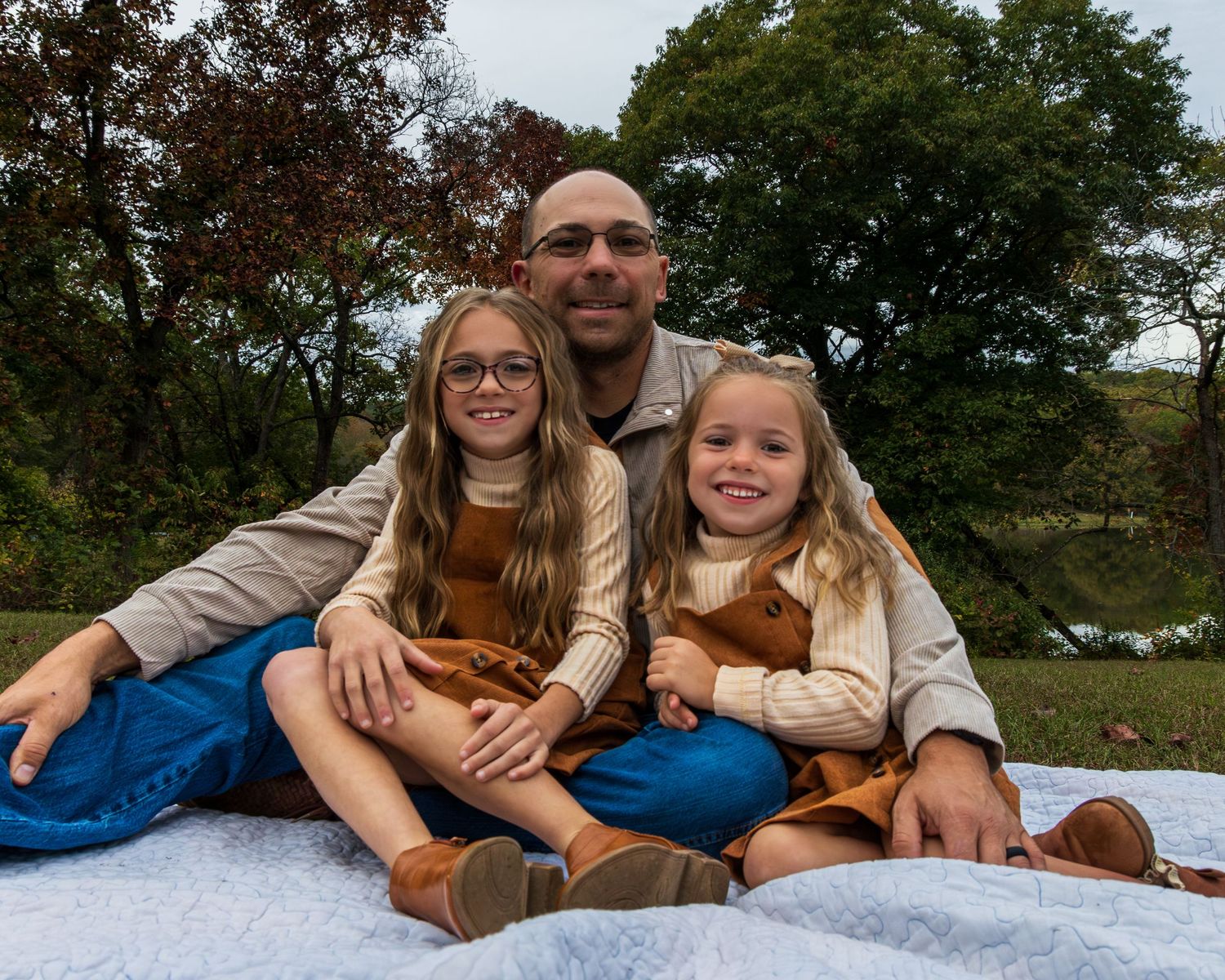 A farther and his two young girls sitting on a blanket.