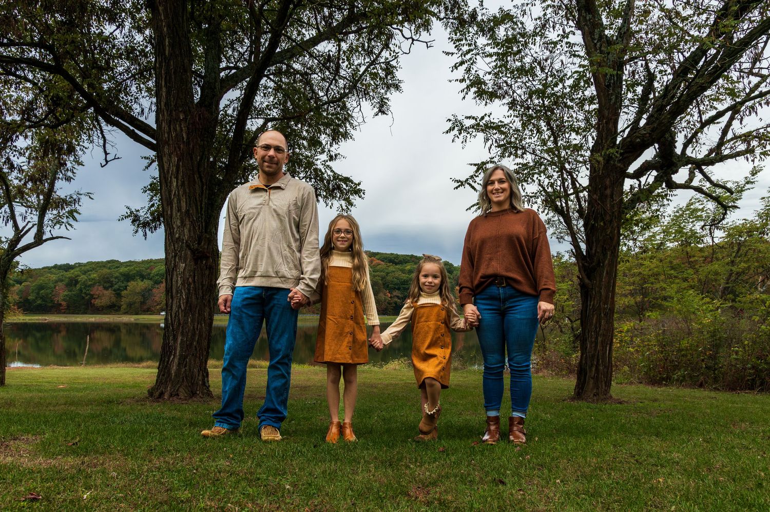 A young family all holding hands standing by a lake.
