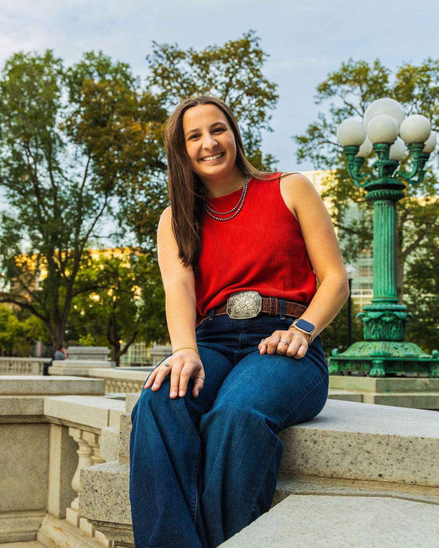 A girl sitting on a stone fence and smiling.