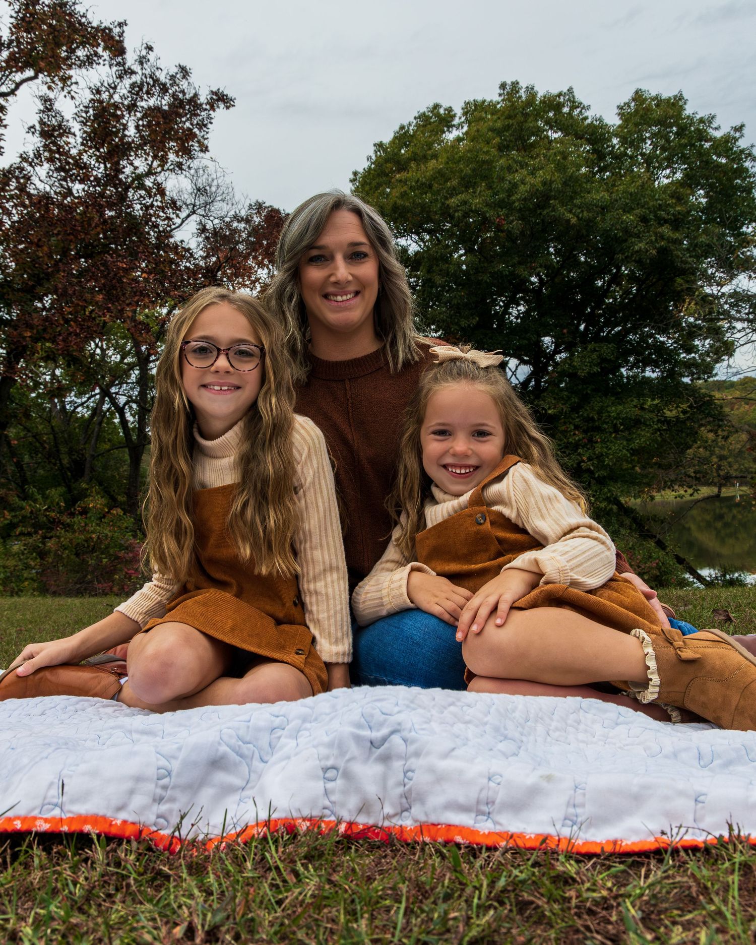 A mother and her two young girls sitting on a blanket.