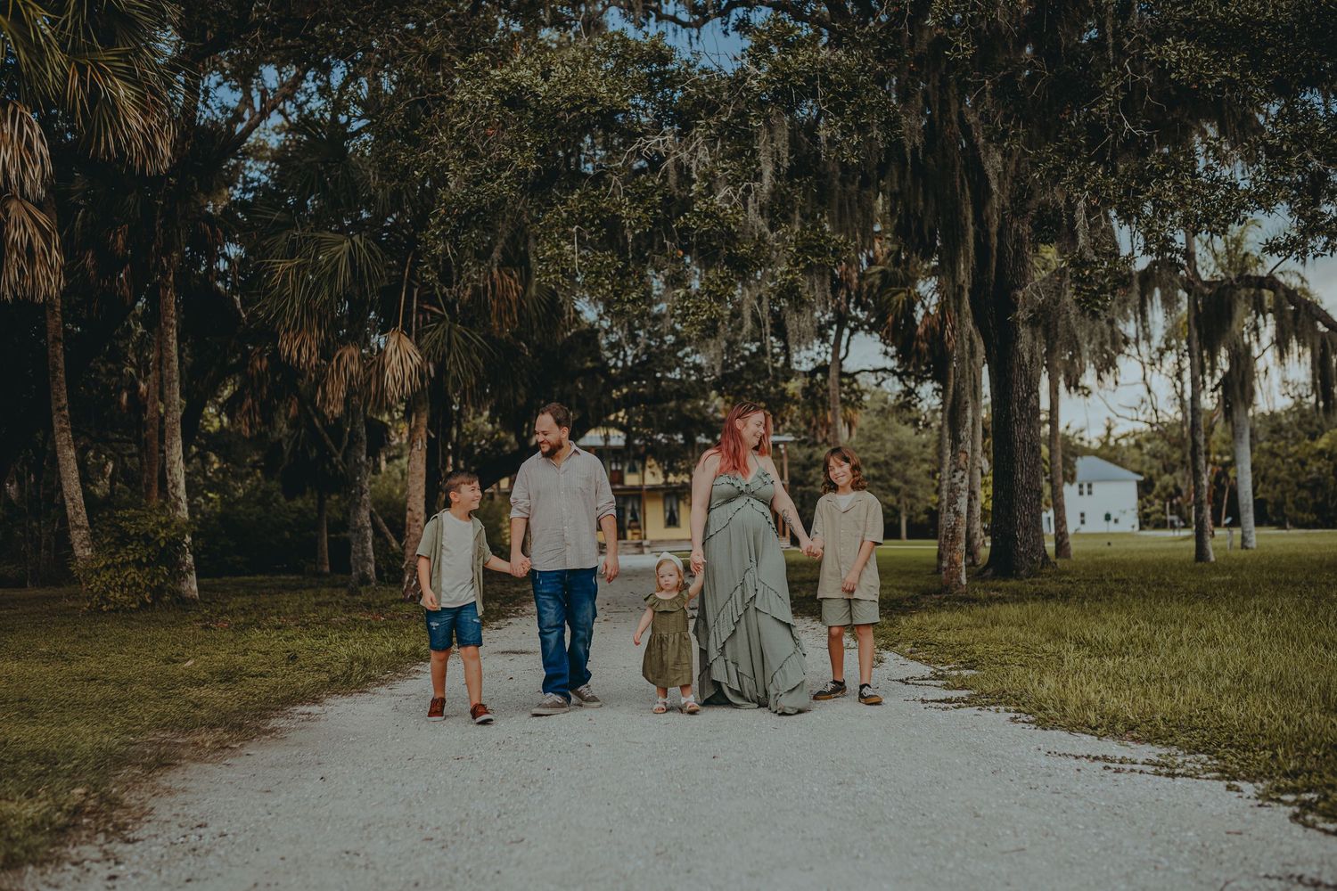 Family of five walking hand-in-hand on a tree-lined path draped with Spanish moss during an outdoor photo session.