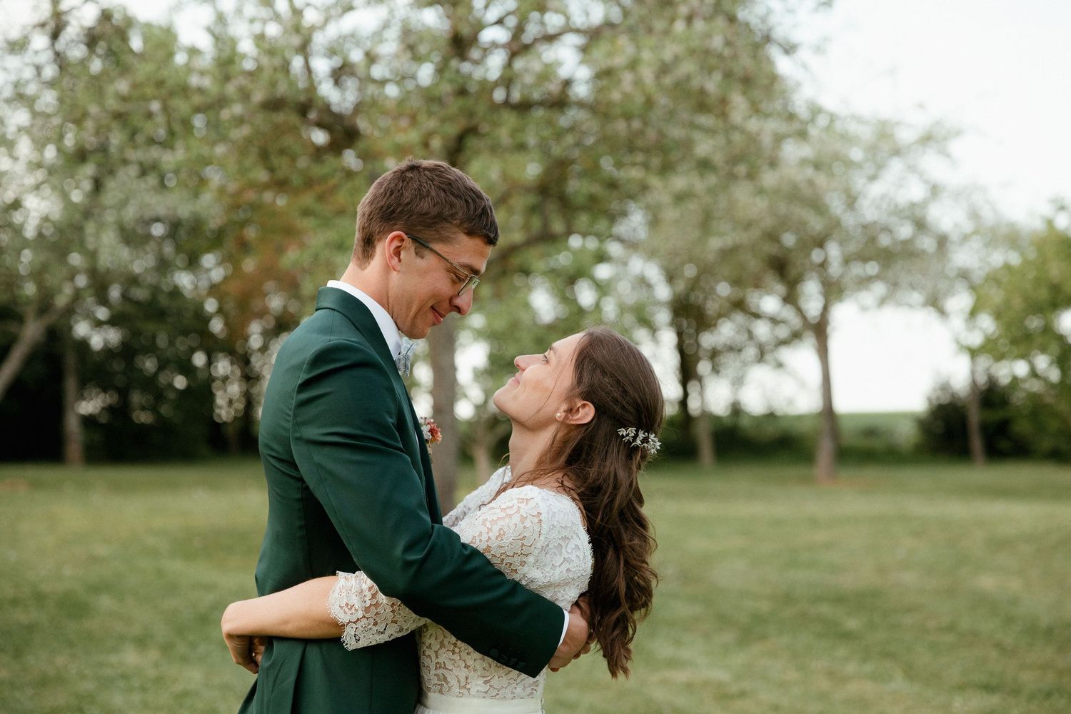 Romantic couple in green attire embrace each other in a beautiful outdoor garden setting during a photo session.