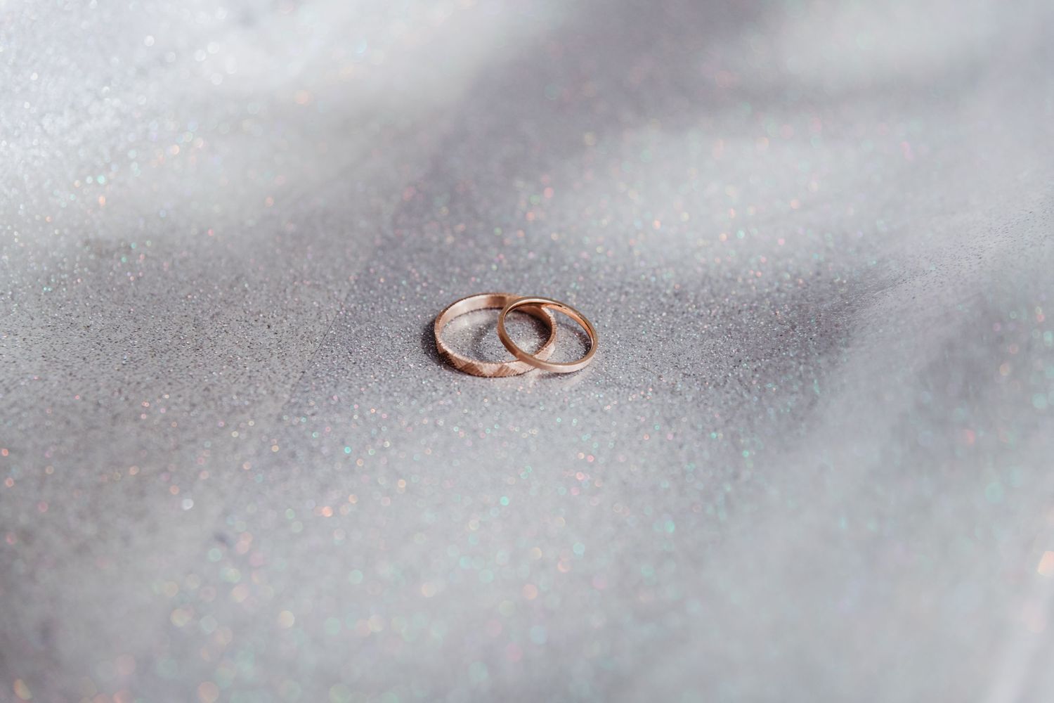 Two gold wedding bands rest side by side on a soft gray textured surface in natural lighting.