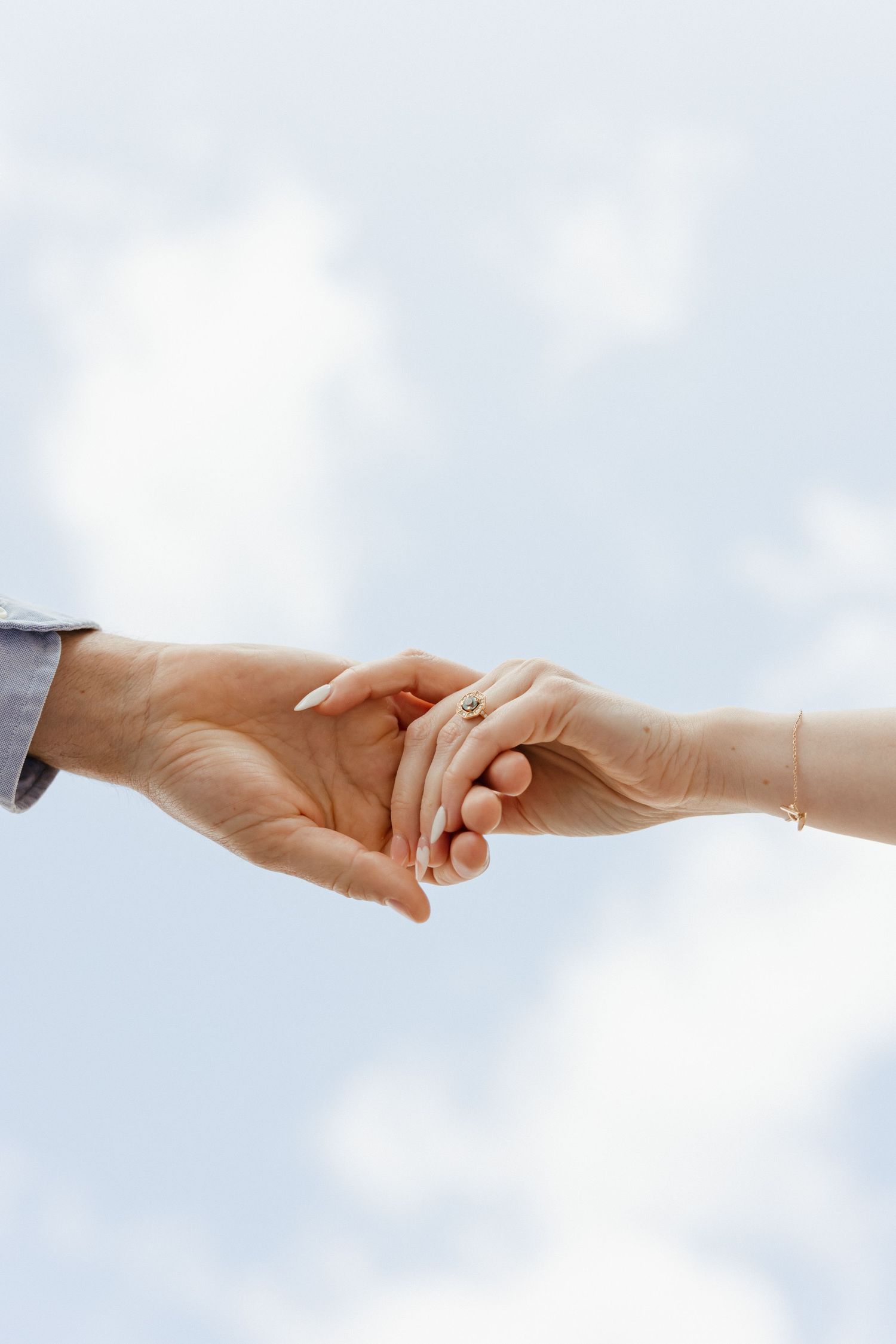 Two hands reach towards each other against a bright cloudy sky background.
