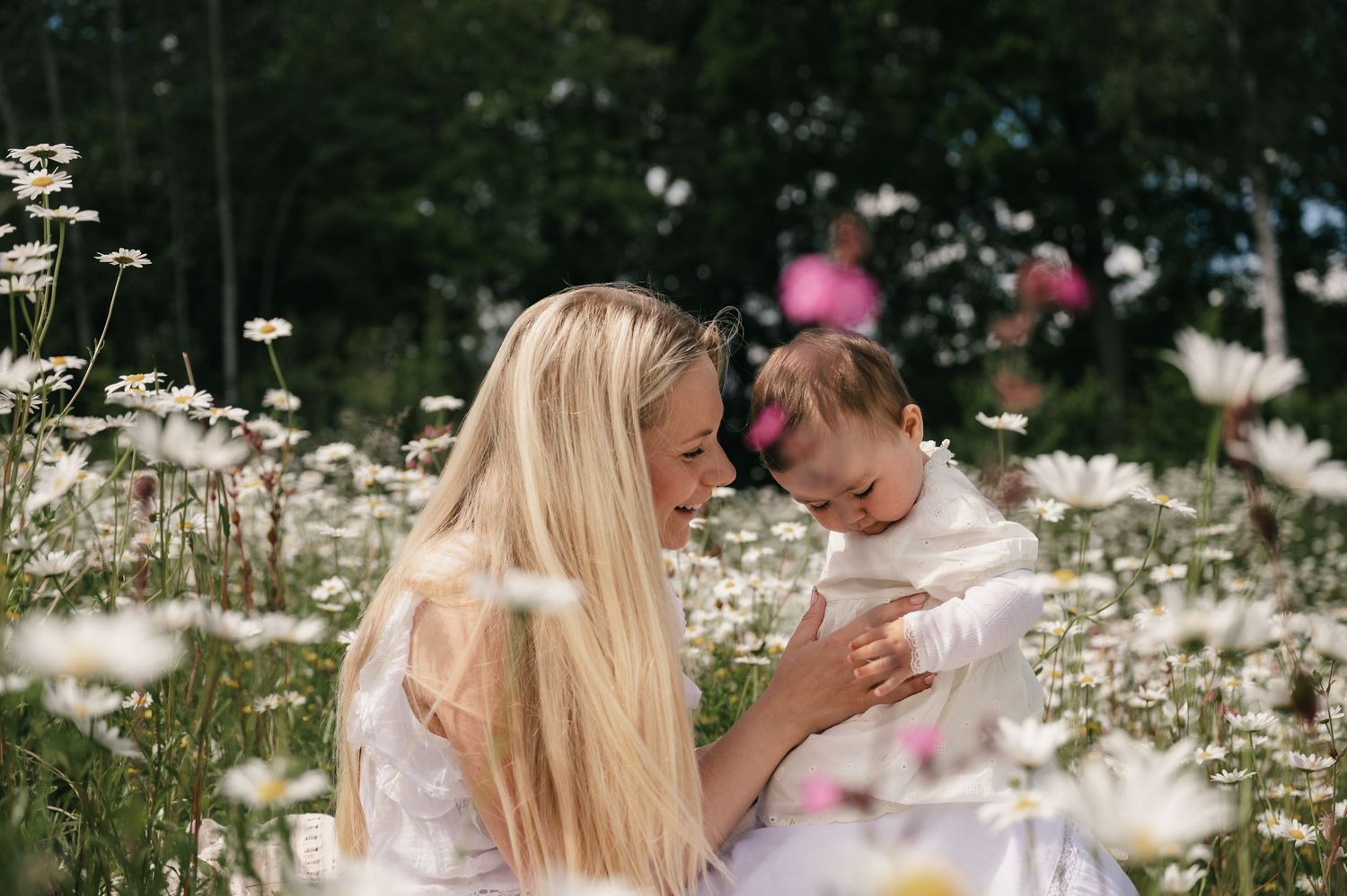 A mother and young child share a tender moment in a blooming wildflower meadow filled with white daisies.
