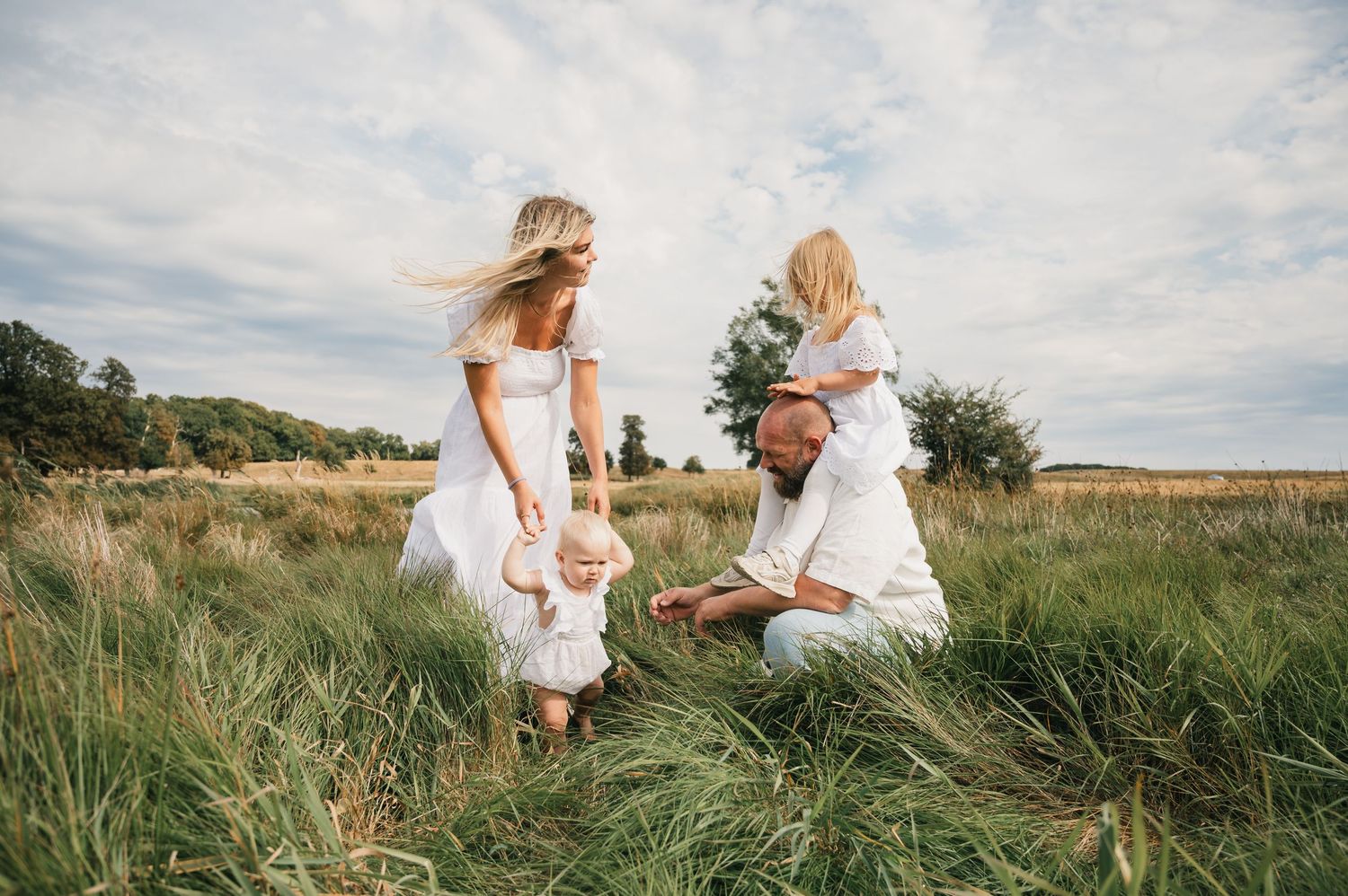 Family in white outfits playing in a green meadow field on a cloudy day.