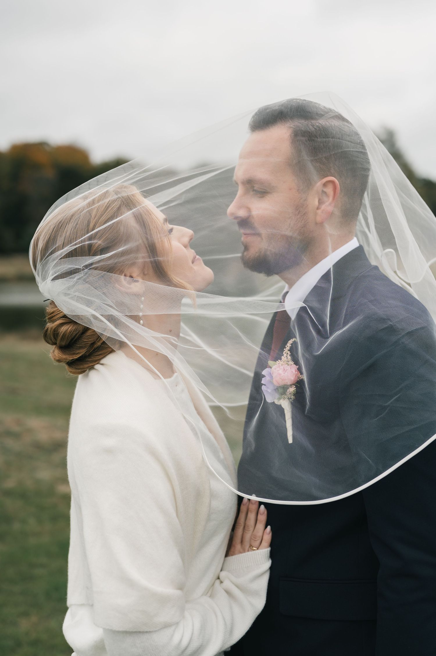 Bride and groom share romantic moment under flowing veil outdoors on their wedding day.