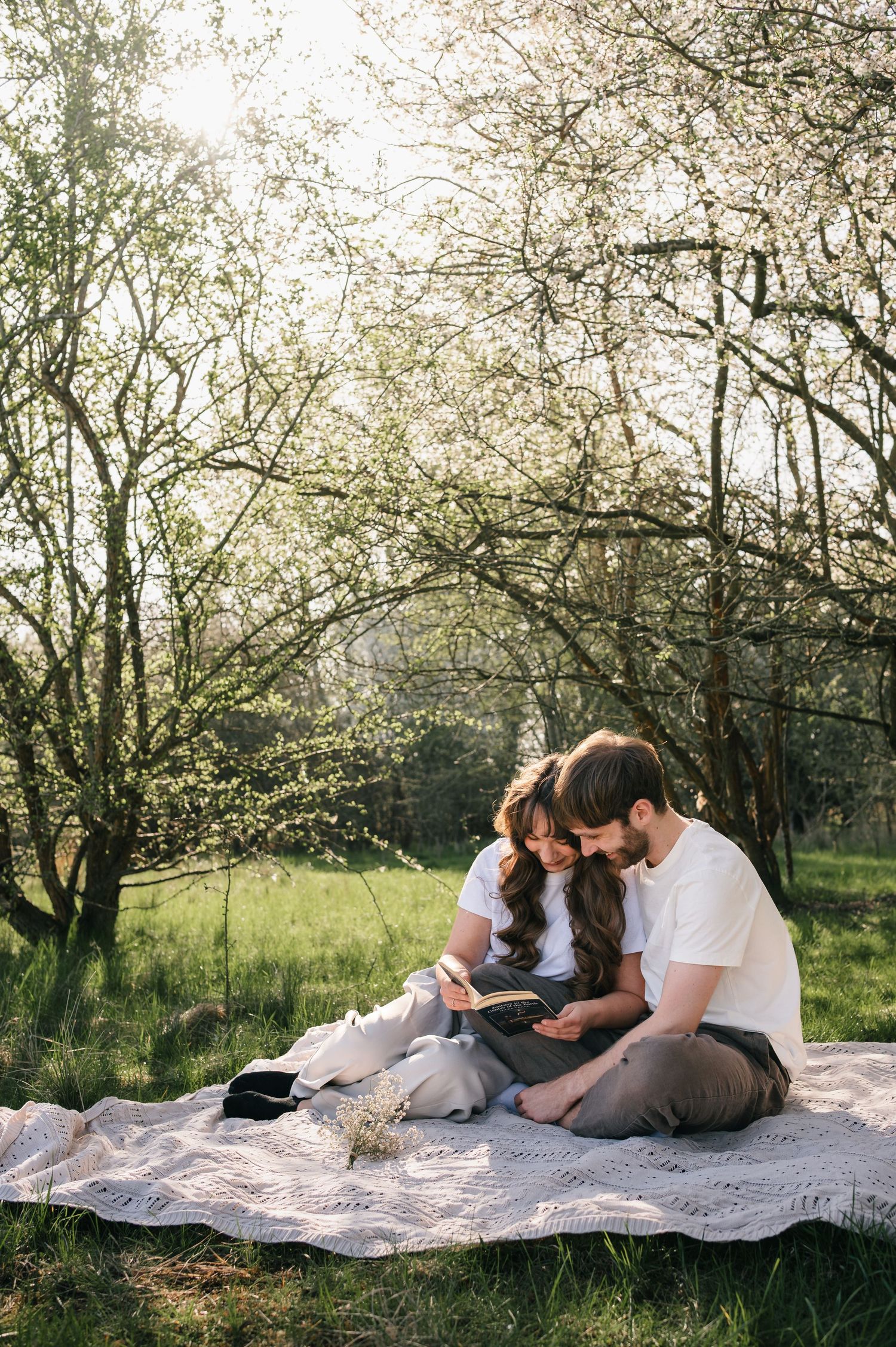 Couple sitting on a blanket in a blooming garden, reading together on a sunny spring day.