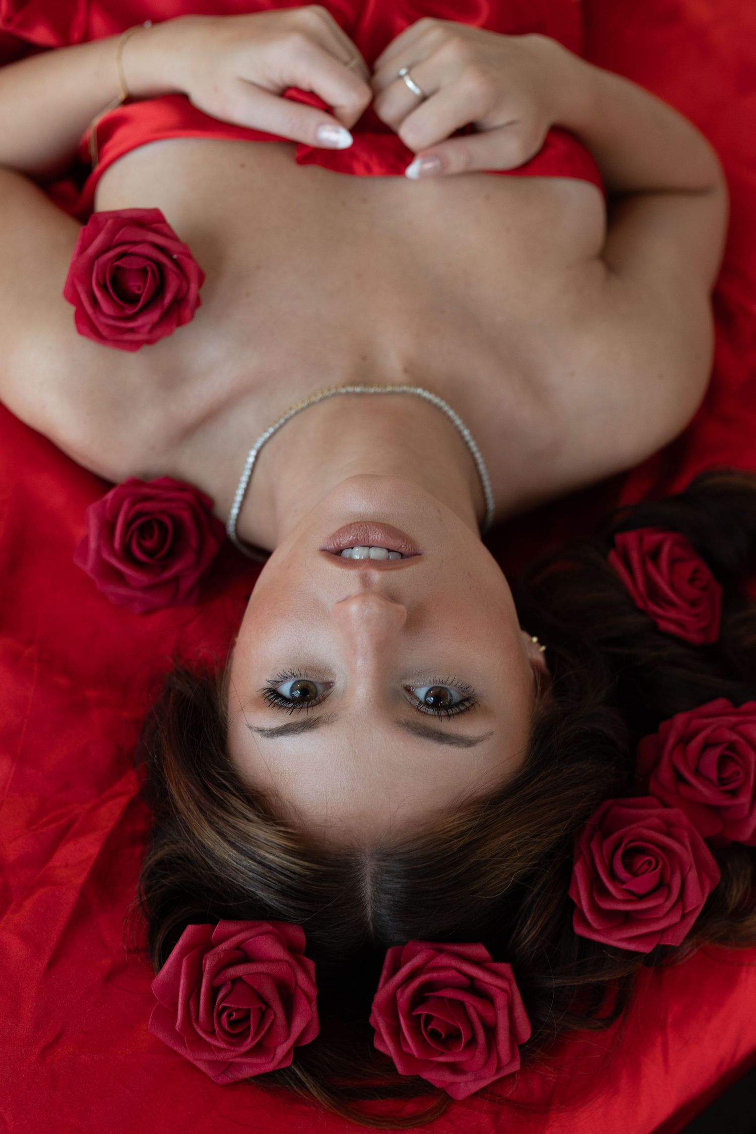 An artistic portrait on red fabric surrounded by vibrant red roses showcasing delicate glamour makeup and jewelry.