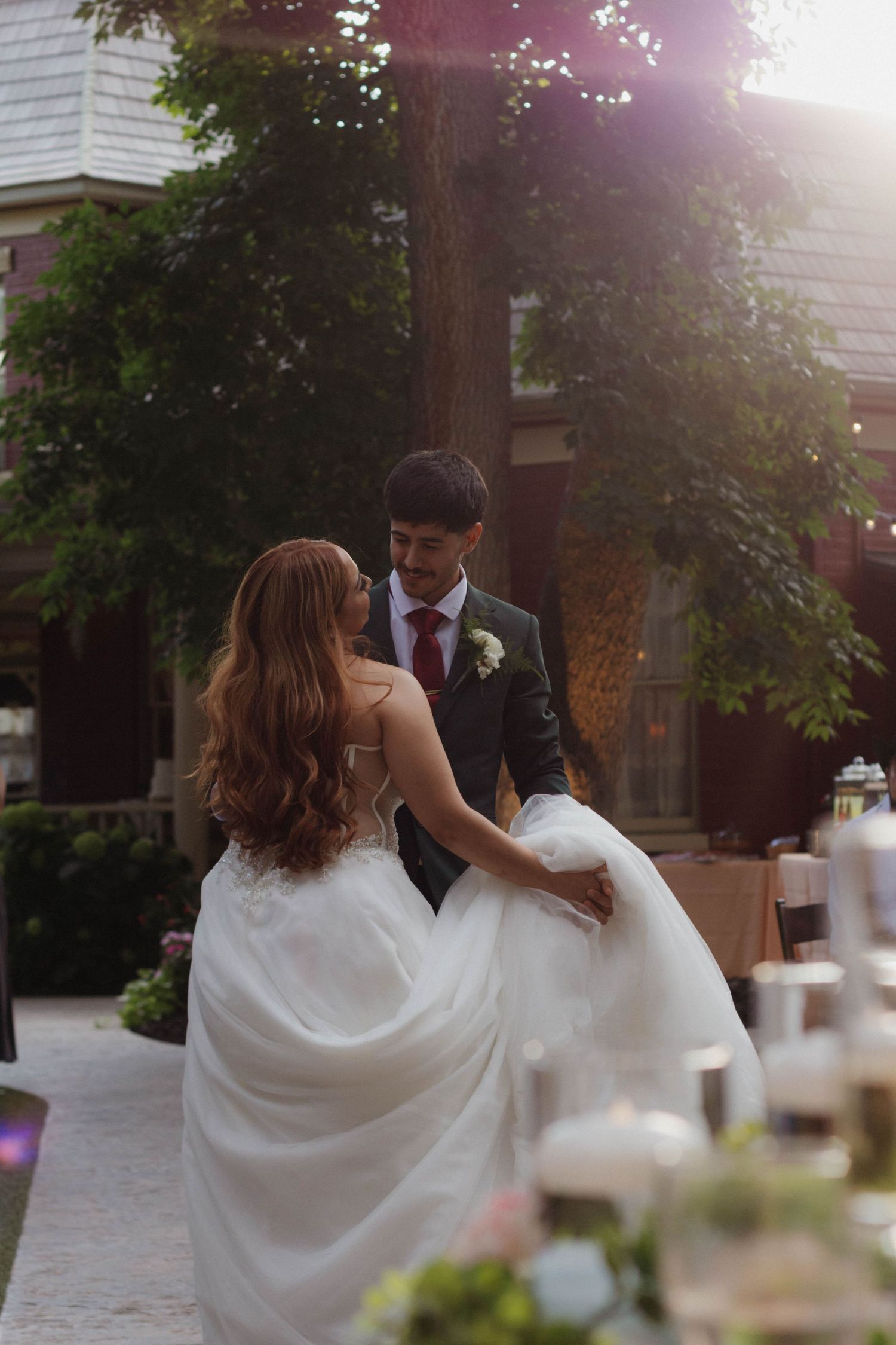 A couple shares a romantic moment outdoors at sunset with soft lighting and decorative elements in the foreground.