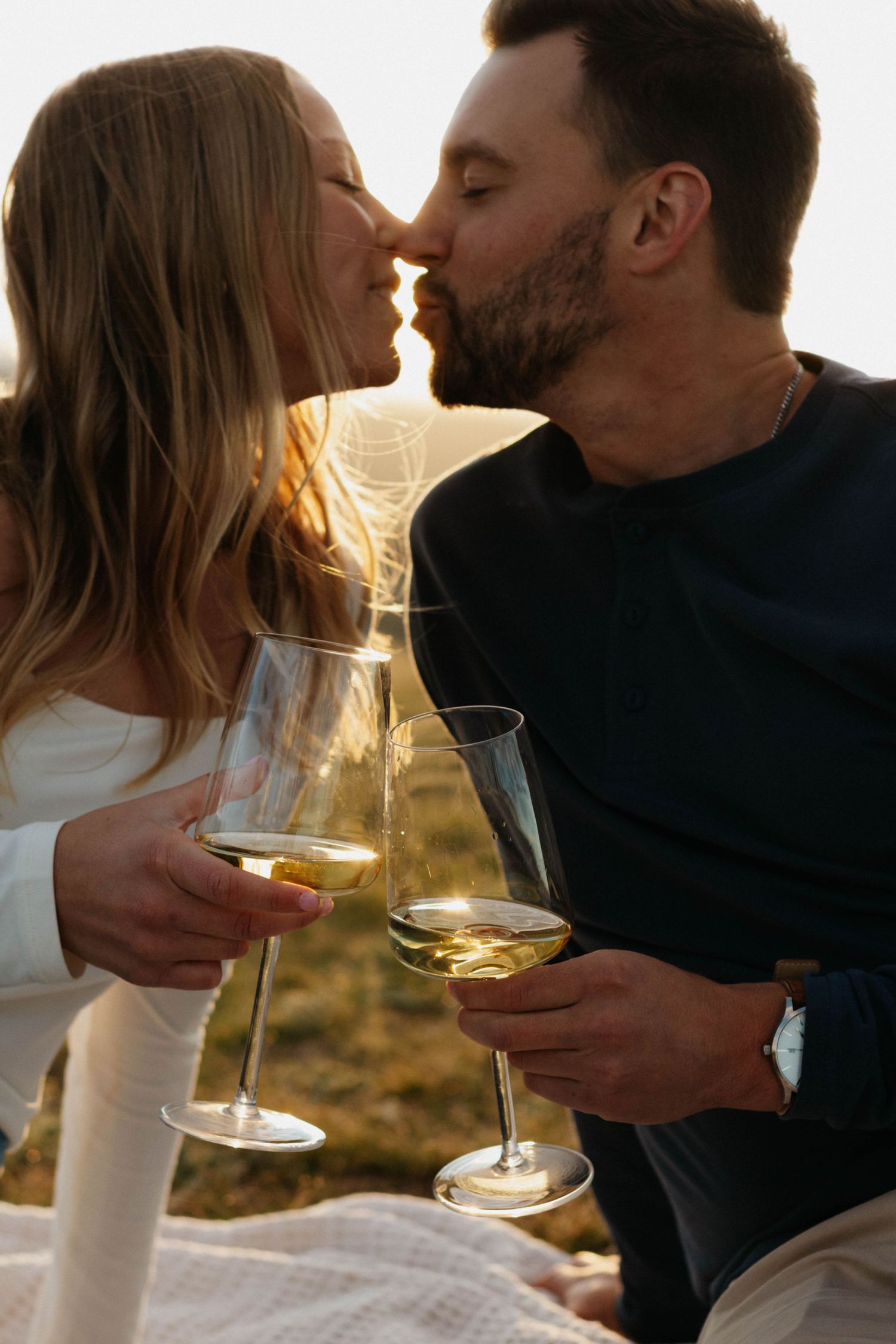 Romantic couple shares intimate moments while holding wine glasses during golden hour sunset.