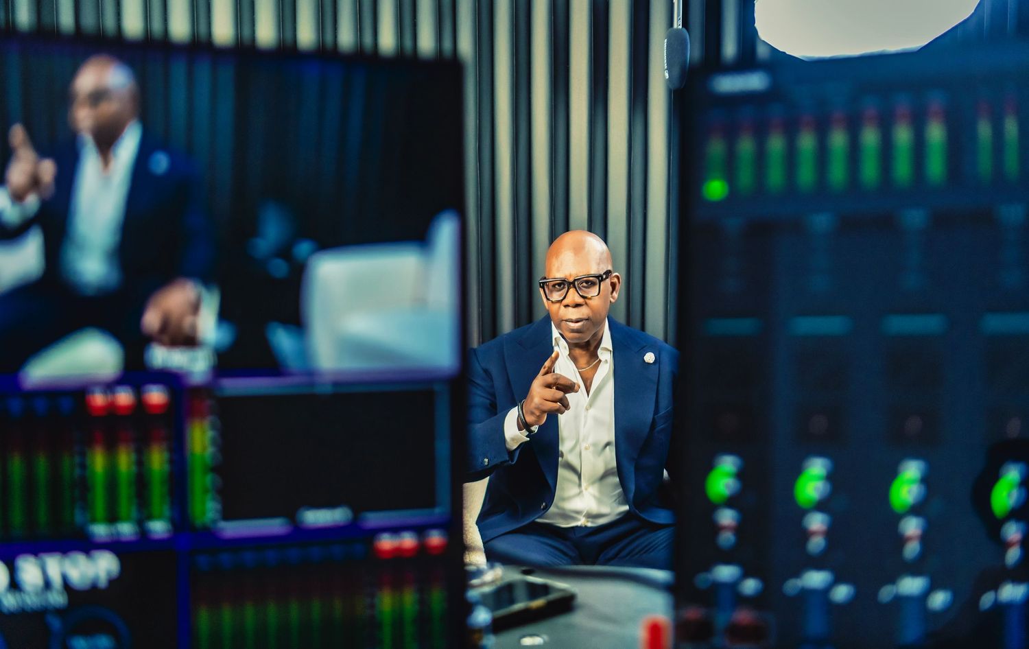 Professional man in blue suit gesturing in a high-tech studio with screens and data displays in background.