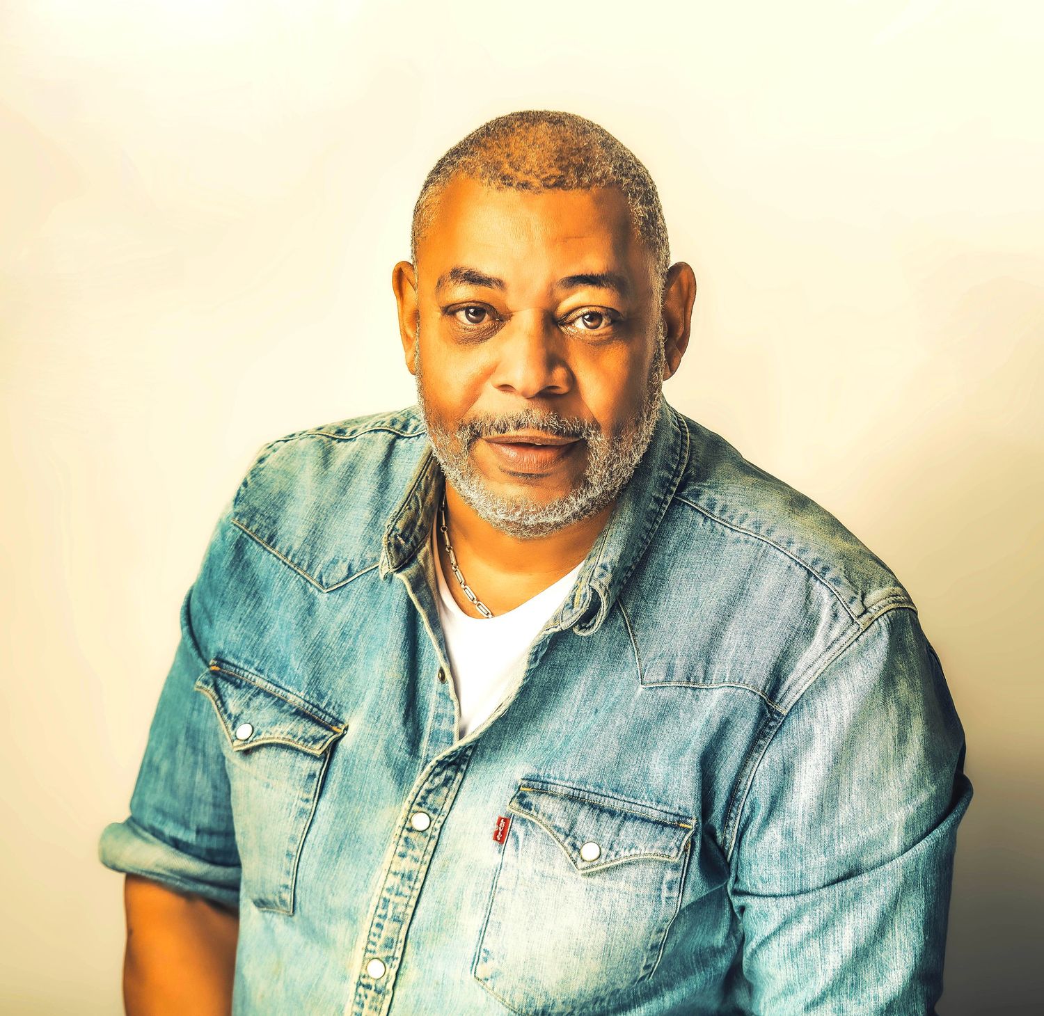 Middle-aged Black man with gray beard wearing a denim shirt, posing confidently against a neutral background.