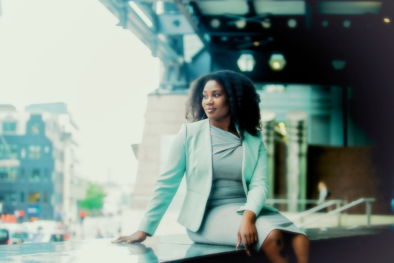 Photography of Black Businesswomen dressed in a Green Mint outfit sitting on a wall with a London City backdrop.