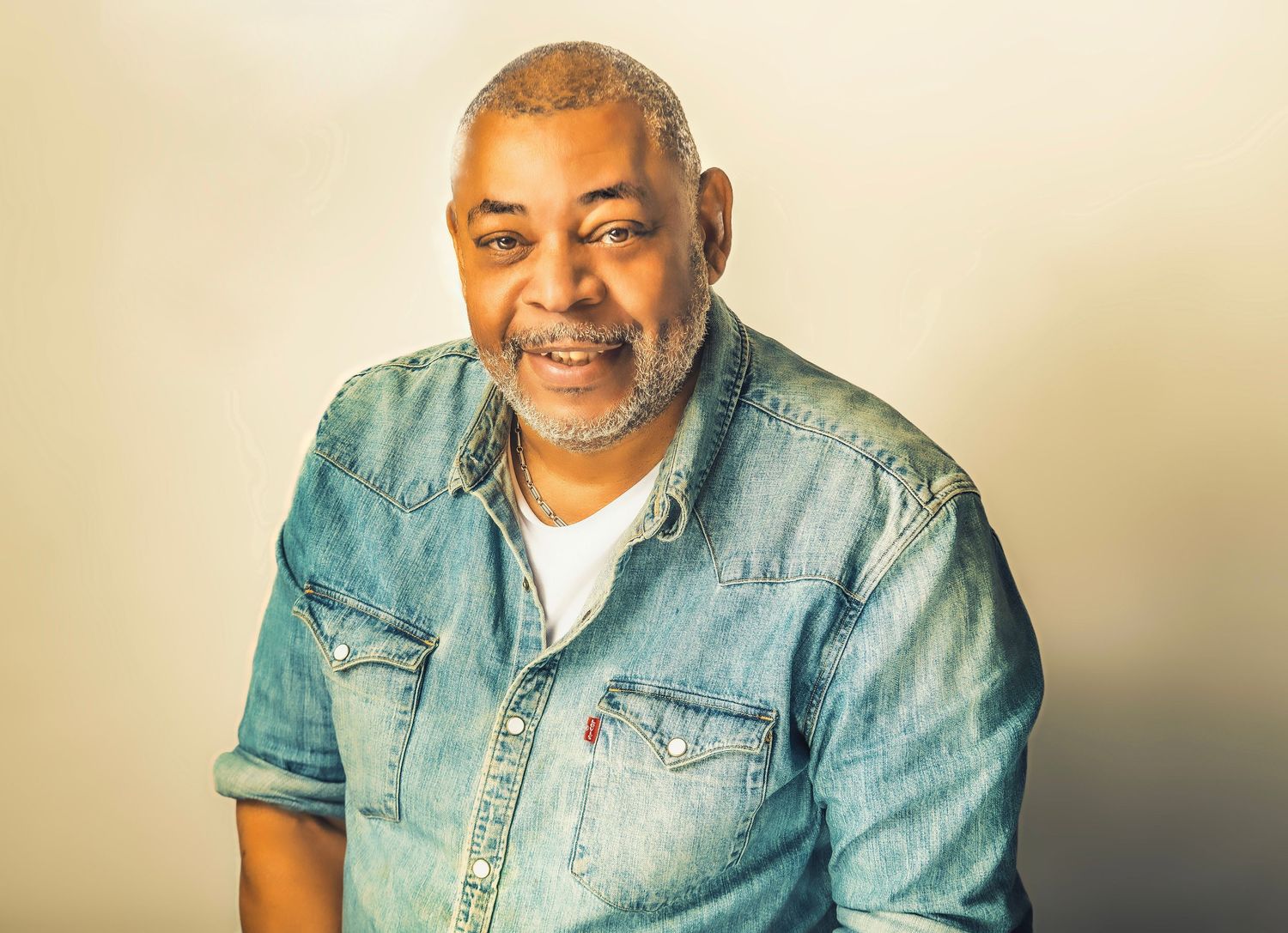 Smiling middle-aged Black man with gray beard wearing a denim Levi's shirt against a neutral background.