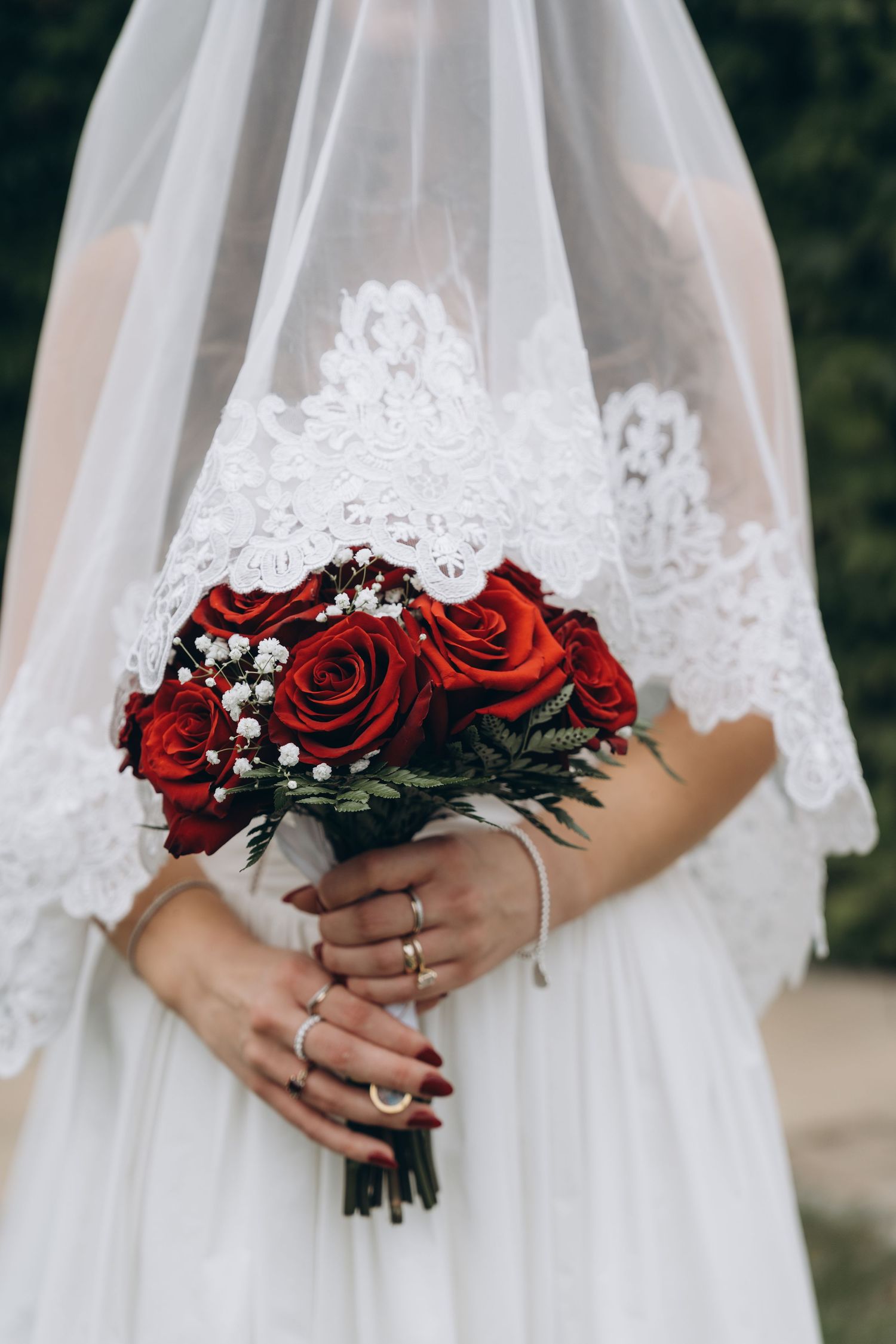 A bride holds a striking bouquet of red roses and baby's breath against her white wedding dress.