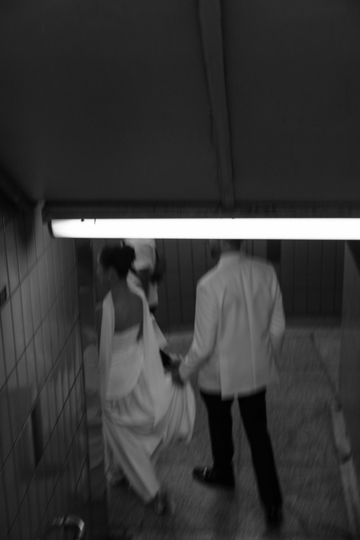 A blurry black and white photo of people walking through a dimly lit underground tunnel with fluorescent lighting.