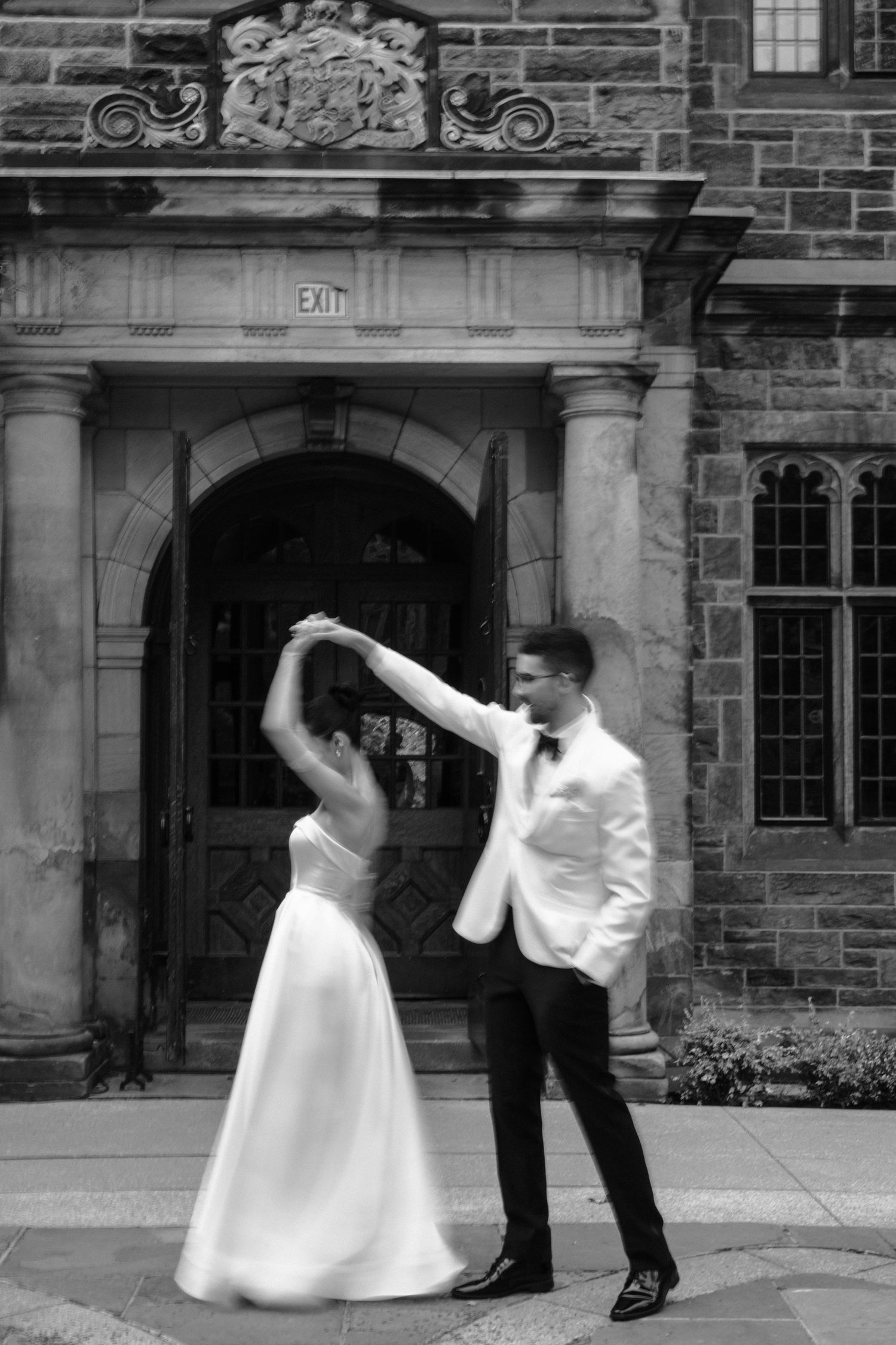 A couple dancing together in front of an ornate stone archway entrance to a Gothic building.