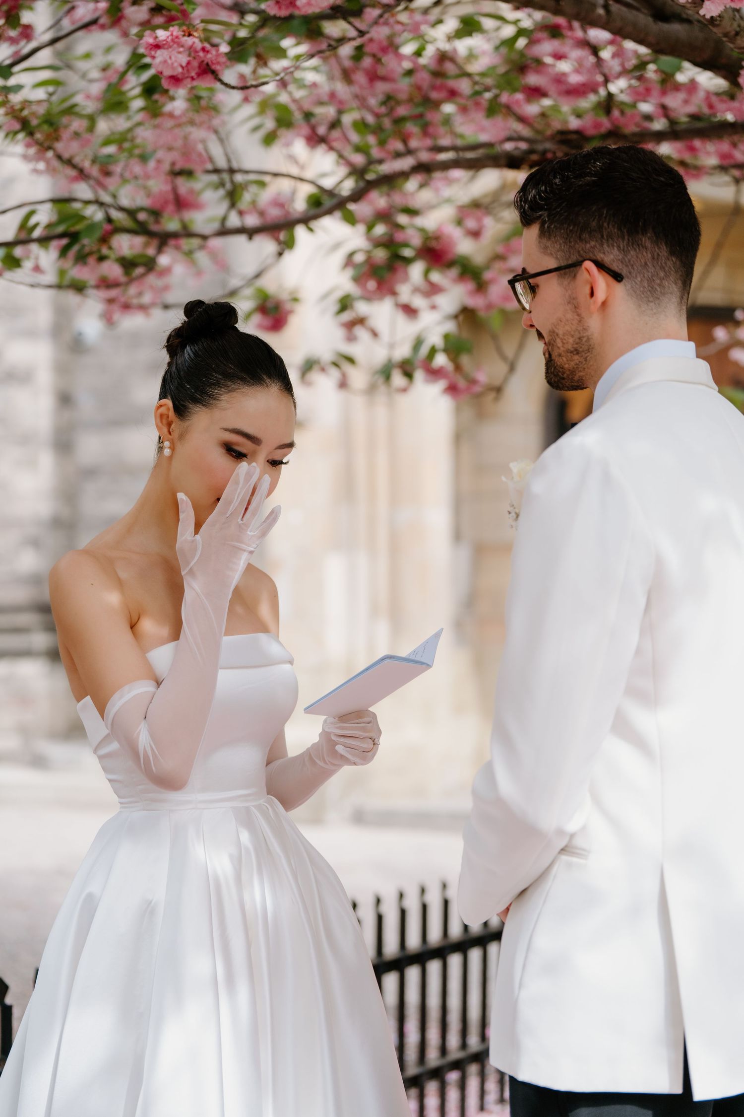 Romantic first look photos of a couple in white under blooming cherry blossoms in springtime.