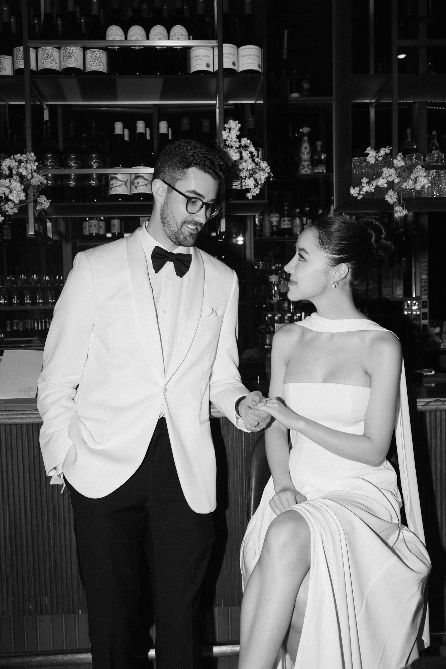 A black and white photo captures a dynamic moment between two stylishly dressed figures at an upscale bar.