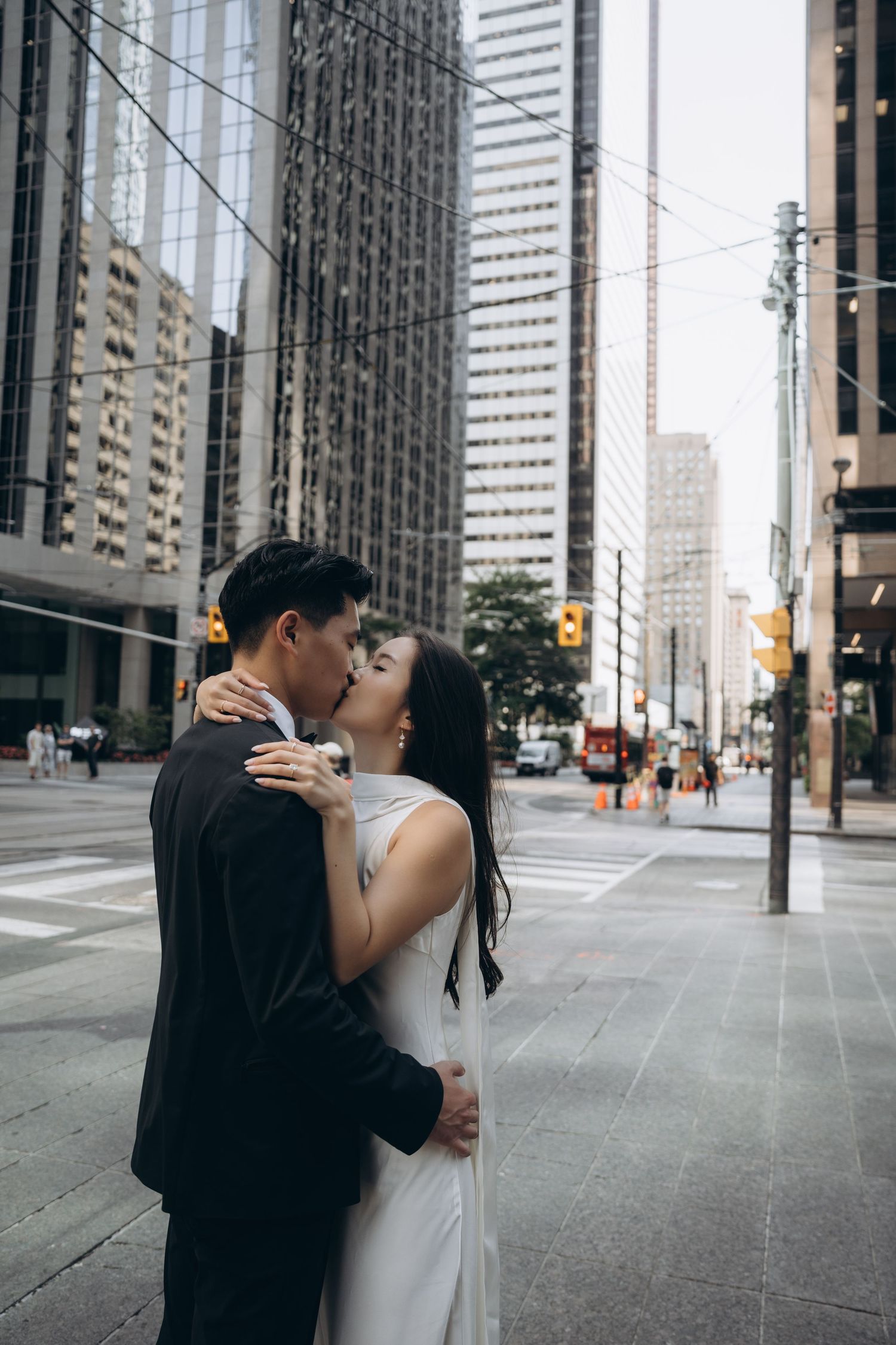 A romantic couple shares an intimate kiss on an empty downtown street with modern skyscrapers in the background.