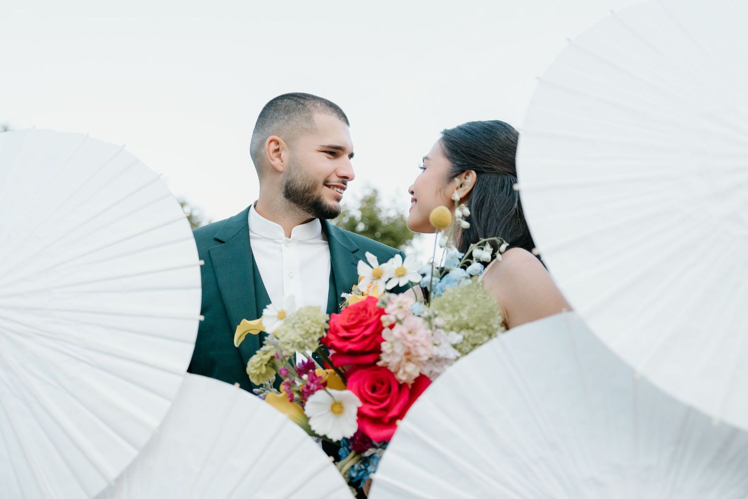 Romantic wedding couple poses with colorful bouquet against sunlit background during golden hour.