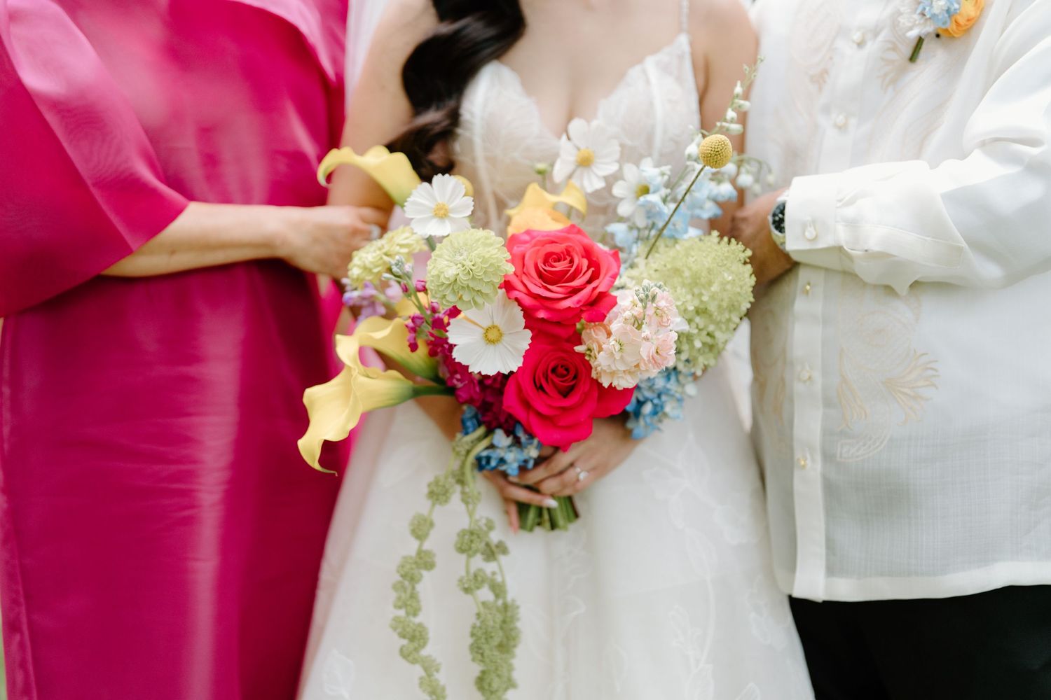 Wedding couple holds vibrant bouquet with pink roses and mixed flowers against white formal attire.