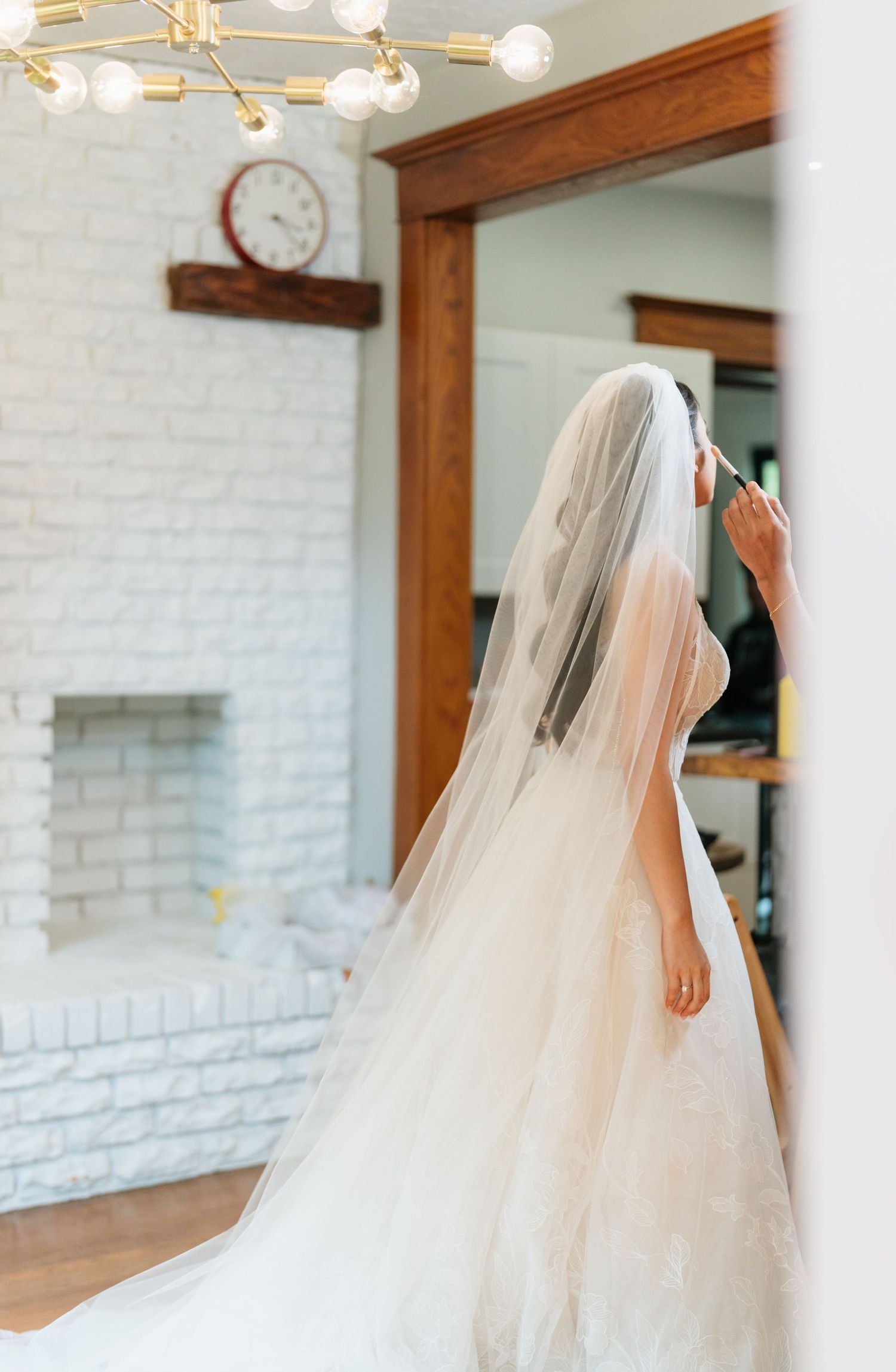 A flowing white wedding veil gracefully moves in a bright interior space with white brick walls and wooden trim.