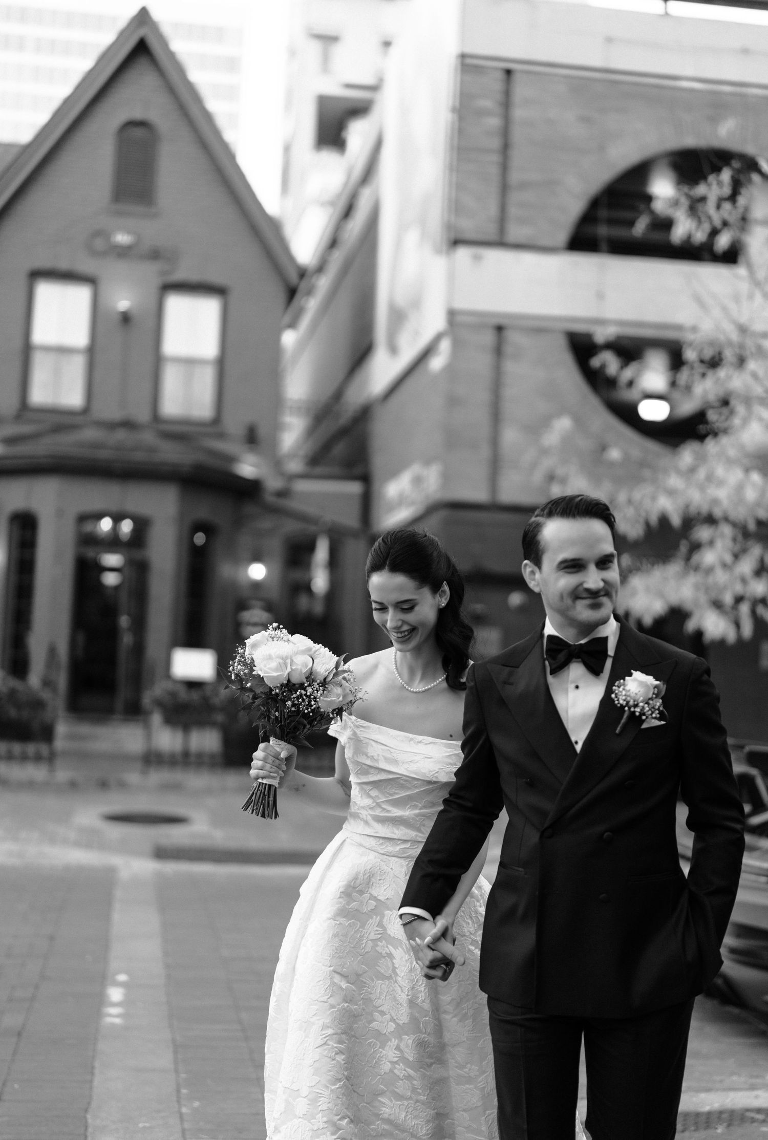 Black and white wedding photograph showing couple walking and laughing together outdoors.