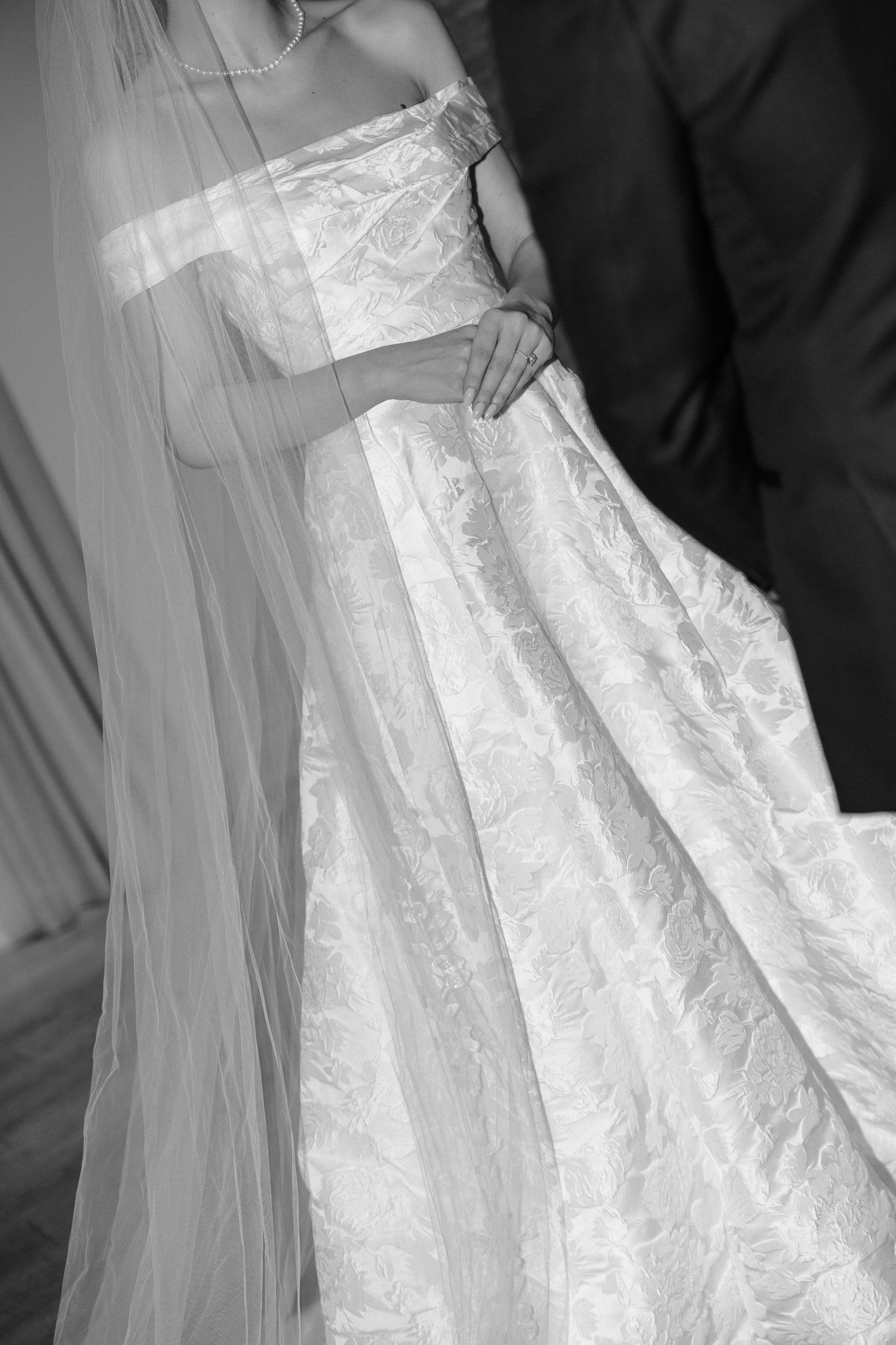 A close-up view of a white lace wedding dress showing intricate details of the fabric and flowing design.