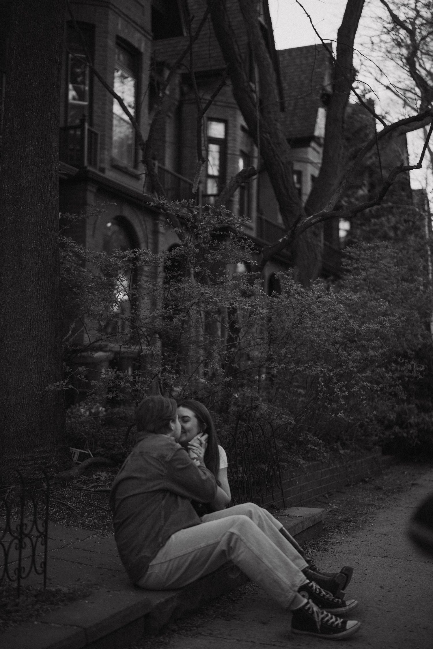 A person sits on a curb outside a gothic-style building in a moody black and white photograph.