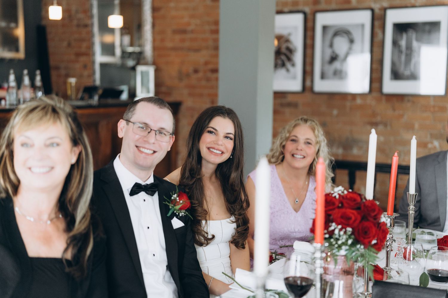 Reception guests enjoying dinner and conversation at elegant tables with exposed brick walls and warm lighting in restaurant setting.