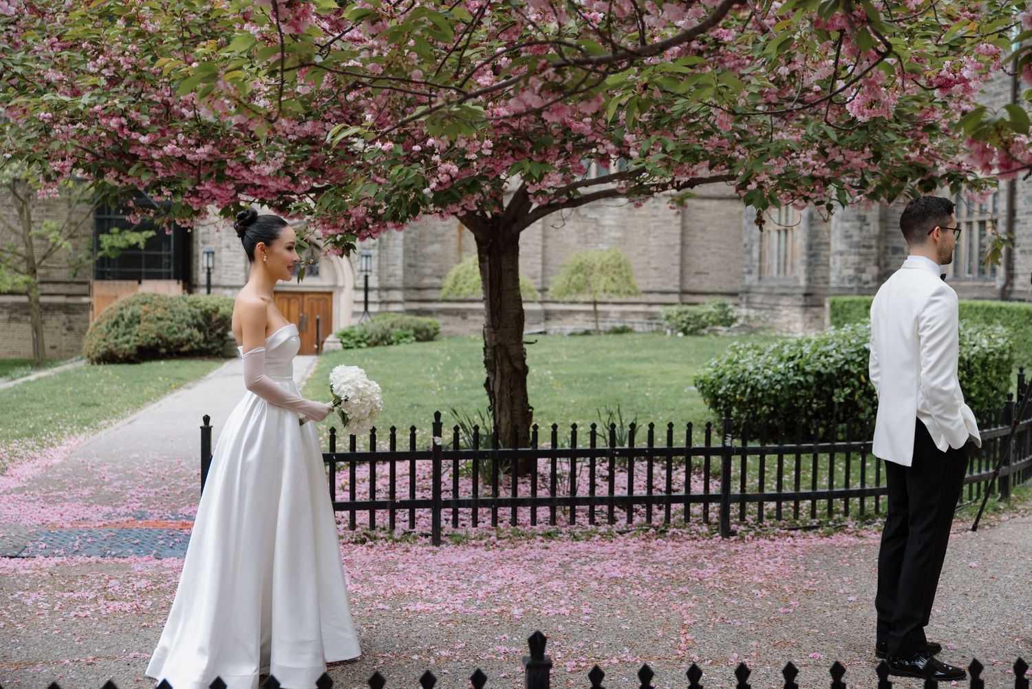 A couple poses under blooming cherry blossom trees in a park setting during a romantic spring photoshoot.