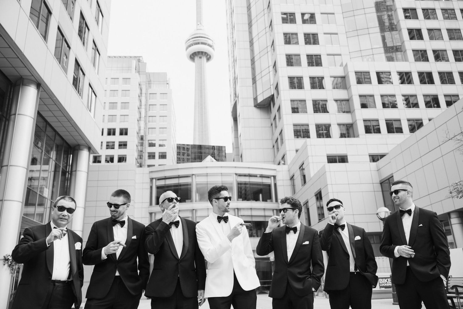 Groomsmen in formal attire pose together on urban street with iconic CN Tower visible in Toronto skyline background.